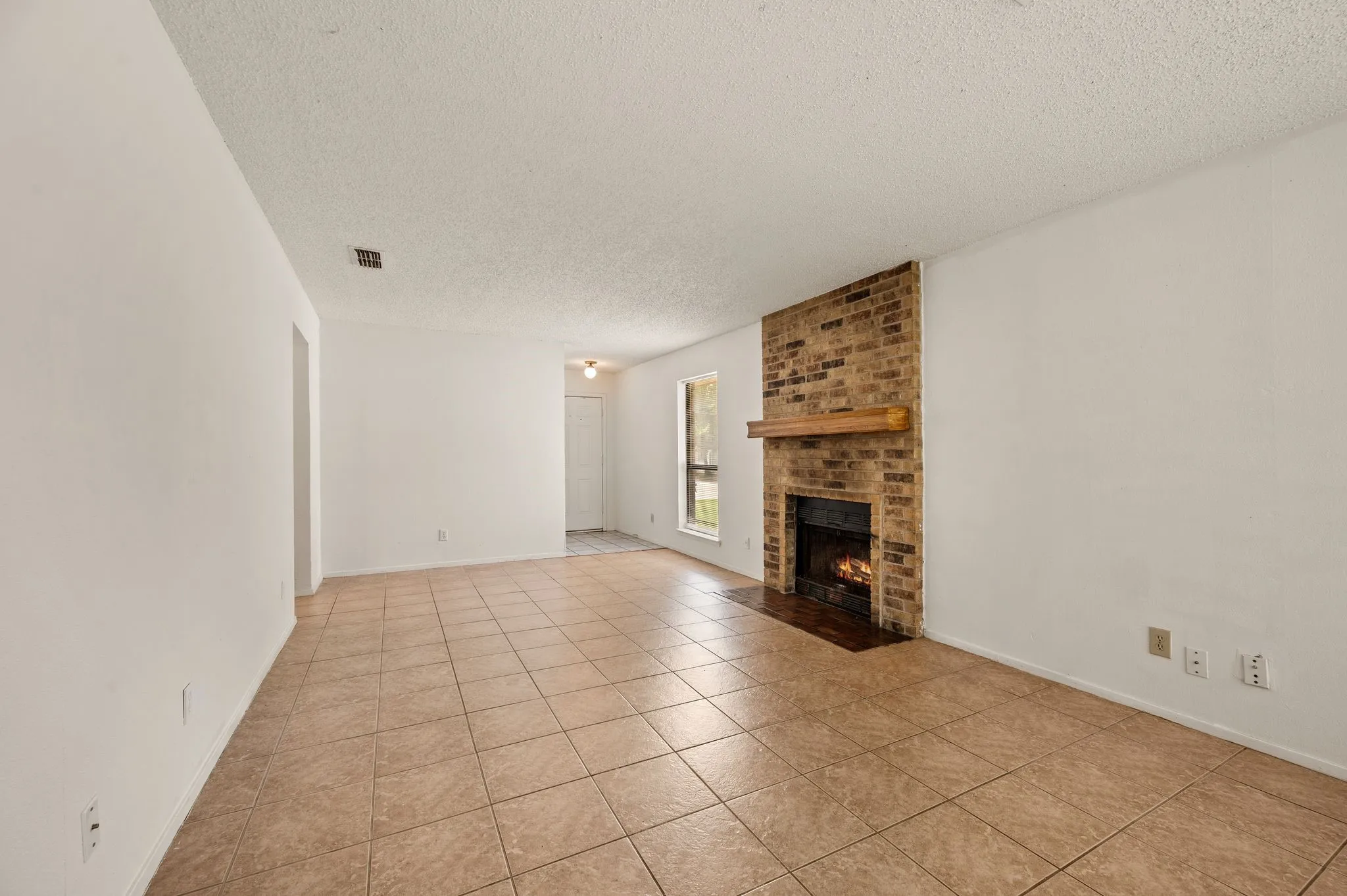 Tiled flooring, exposed brick fireplace with wood mantel, and white painted walls