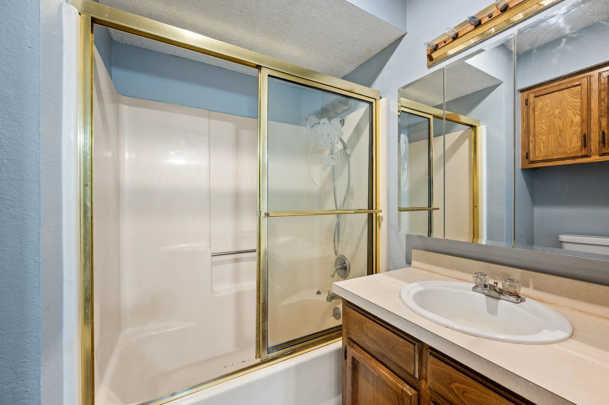 Full shower-tub combination with sliding glass doors, a vanity with an integrated sink, and an overhead mirrored medicine cabinet