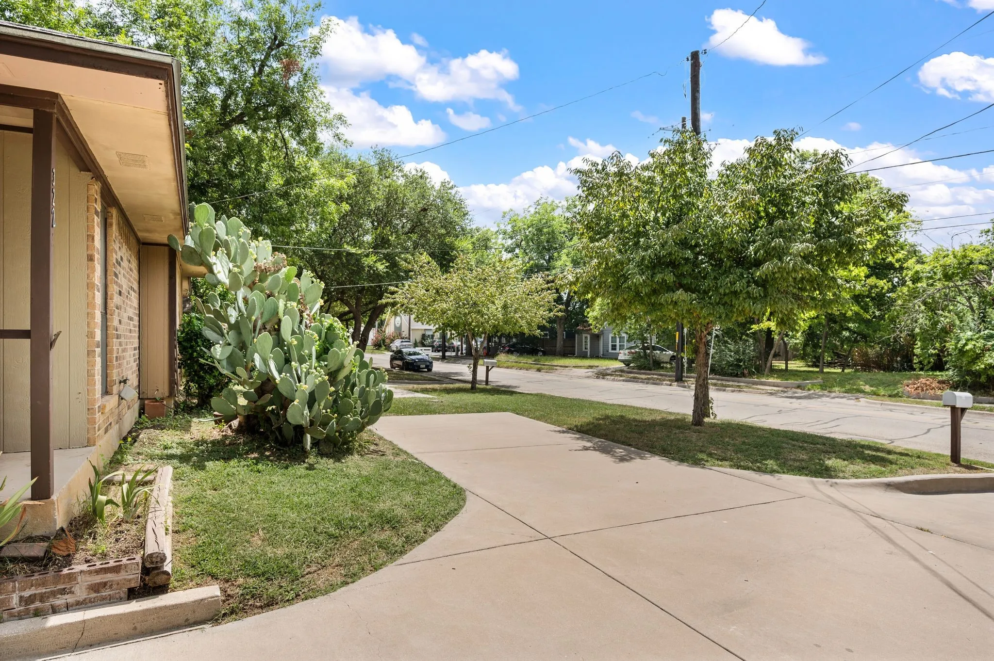 Concrete driveway with a manicured lawn, mature trees, and a brick exterior
