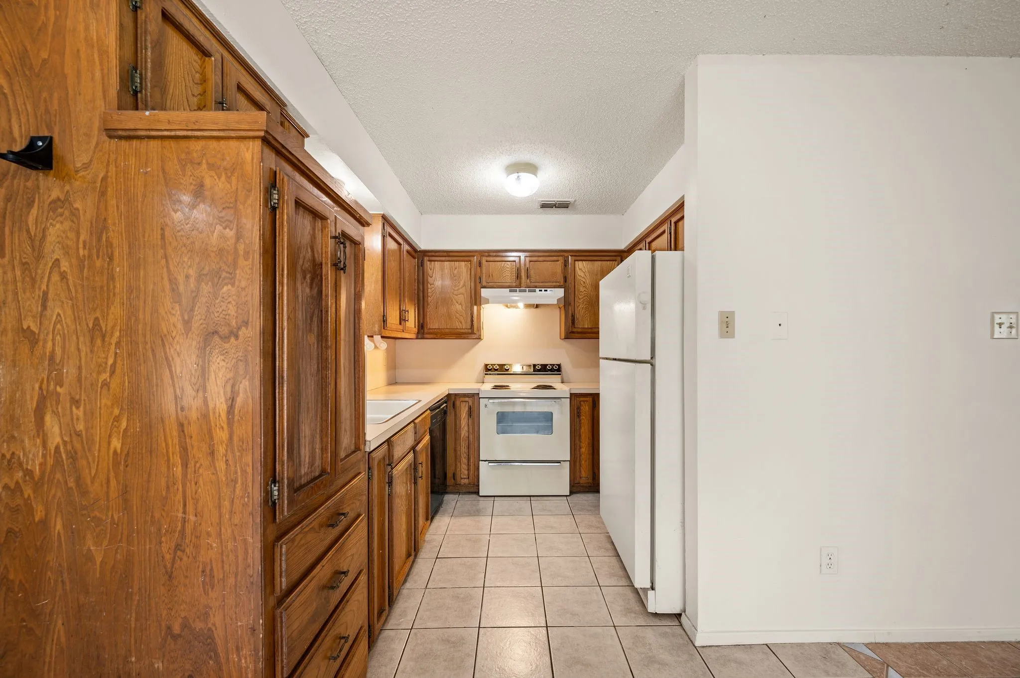 Tile flooring, wood-finish cabinetry, white countertop, white appliances.