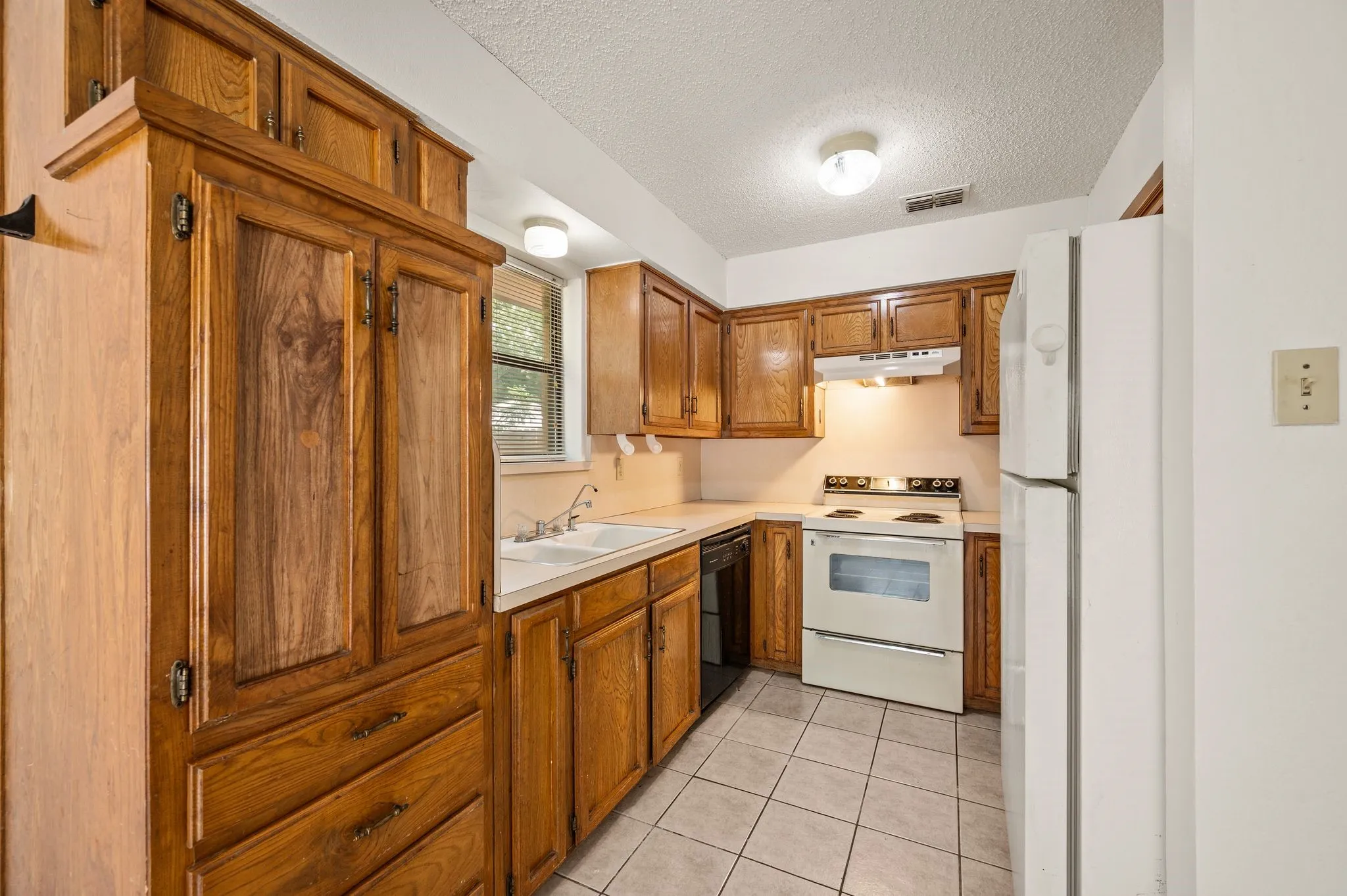 Kitchen featuring extensive wood cabinetry, white countertops, a double basin sink, and tile flooring