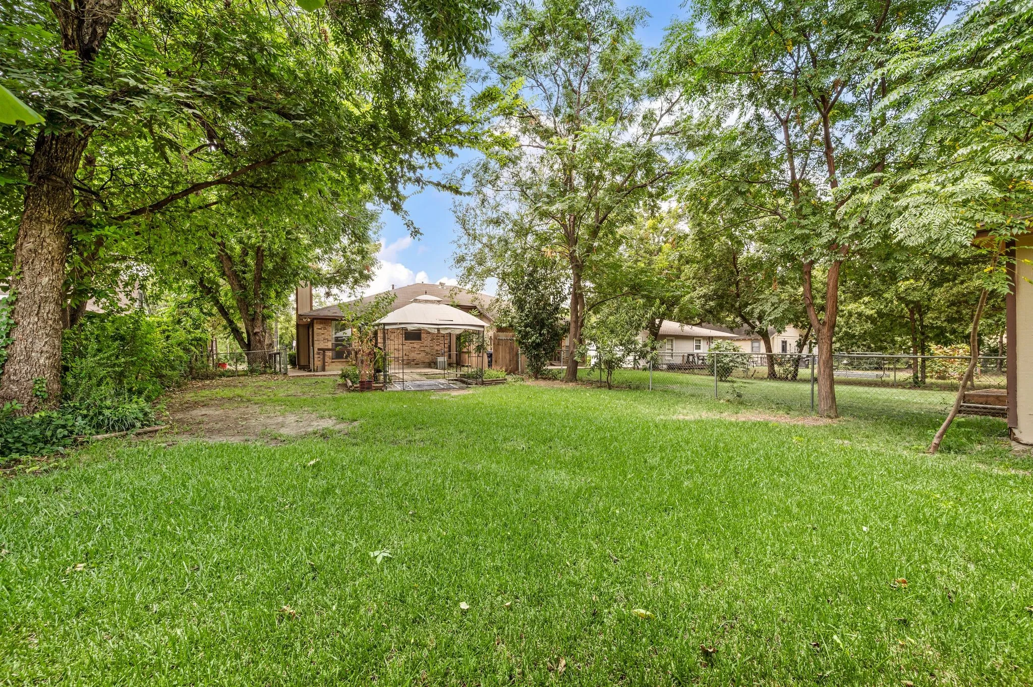 Expansive green lawn with mature trees and a gazebo-covered patio