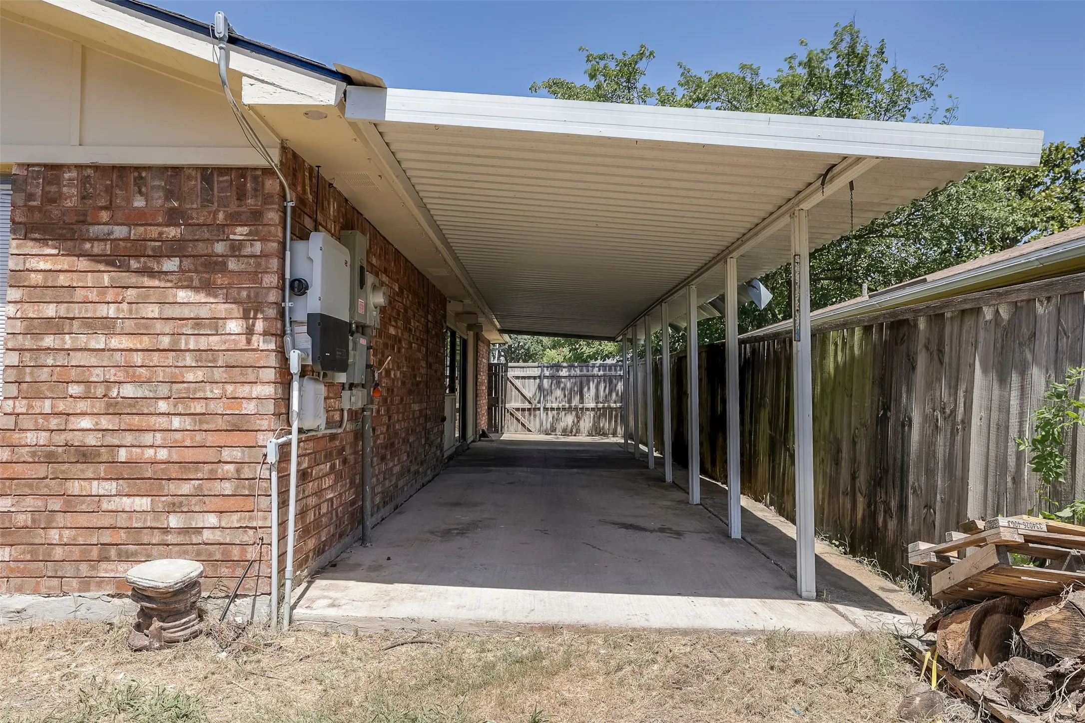 Attached carport with a concrete slab, brick exterior, and wood fencing