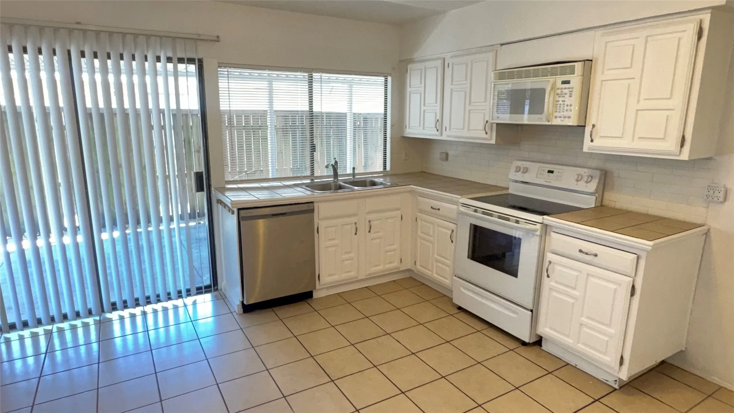 Kitchen featuring white cabinetry, tile countertops, tile flooring, and a stainless steel dishwasher