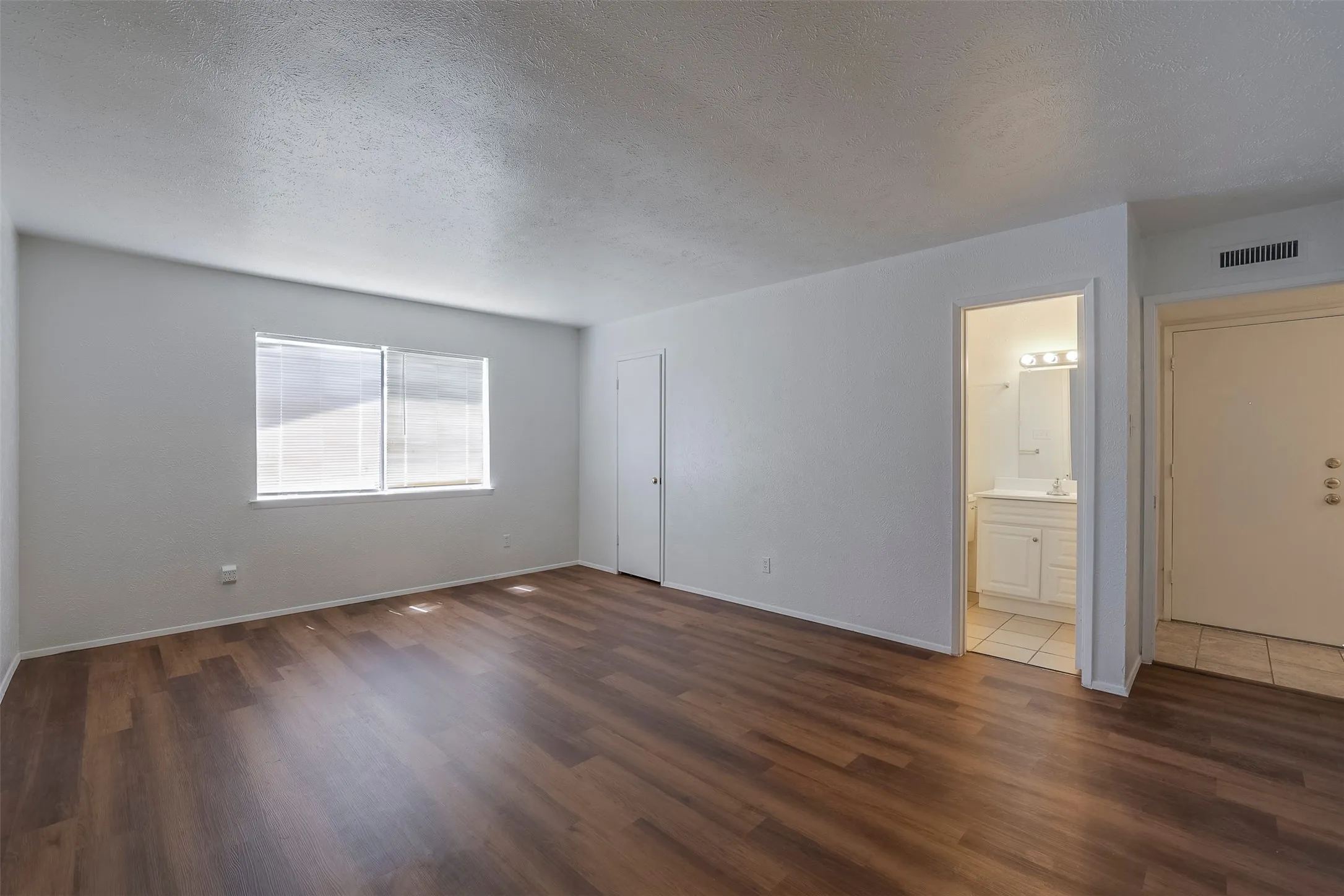 Spacious room featuring rich wood-finish flooring, abundant natural light from dual windows, and clean white walls with neutral trim