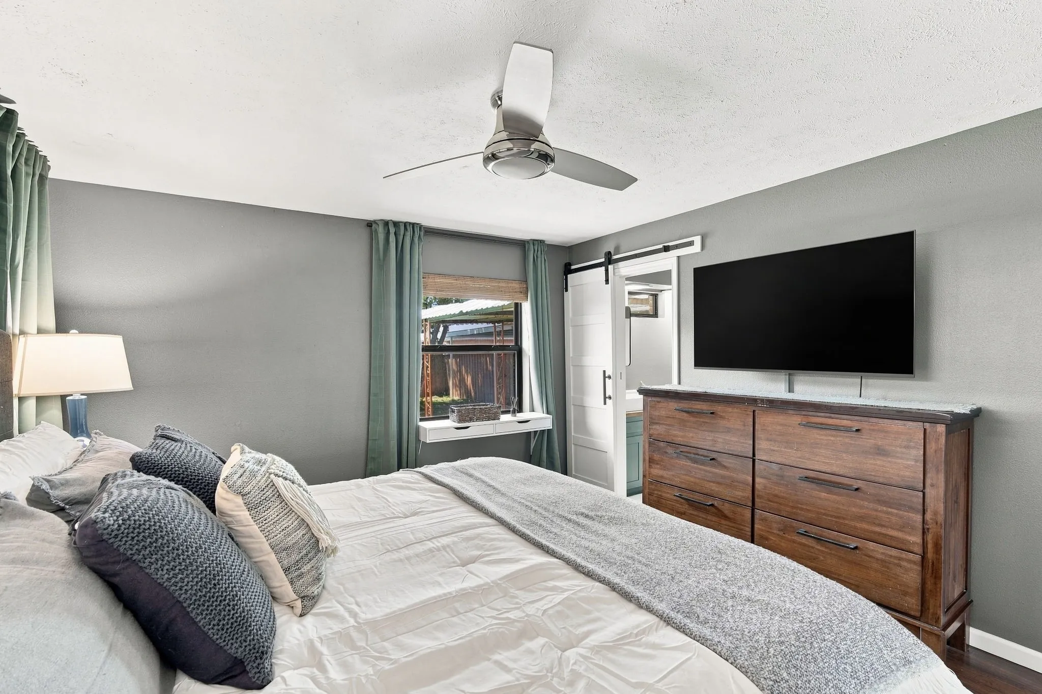 The extra touches are what makes this primary bedroom special. Check out the built in shelf, cool blinds and the barn door to the en-suite bath.