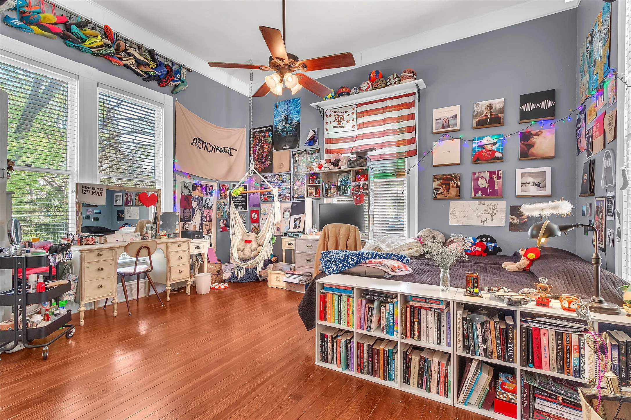 Bedroom with hardwood flooring, eclectic decor, large windows providing natural light, and a wall-mounted bookshelf filled with books and art displays