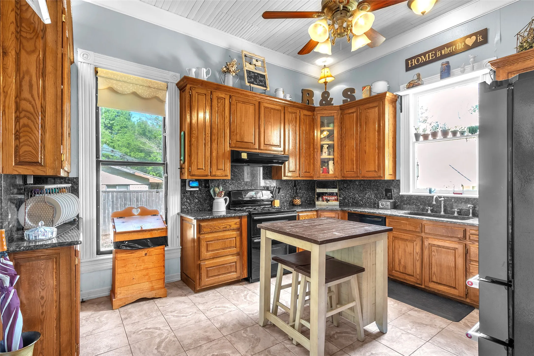 Open-plan kitchen with oak cabinets, black granite countertops, stainless steel appliances, and natural light from large windows.