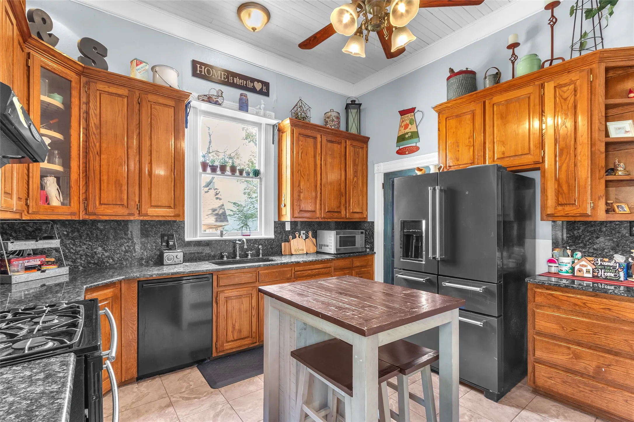 Open-plan kitchen with hardwood cabinetry, black granite countertops, stainless steel appliances, and recessed lighting under a vaulted ceiling
