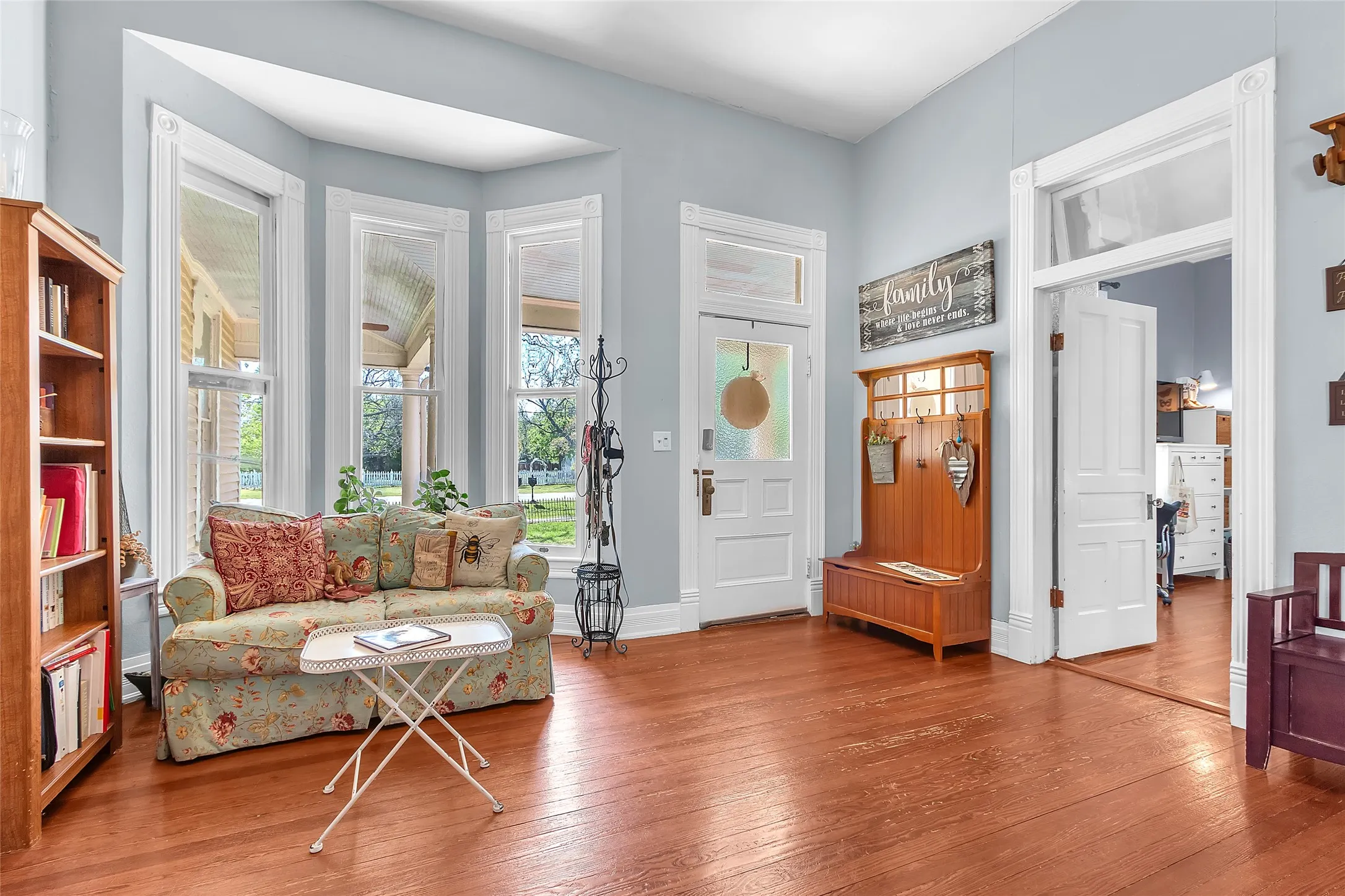 Living room with bay windows, hardwood flooring, vintage-style furniture, and a warm, inviting layout from natural light streaming through the windows