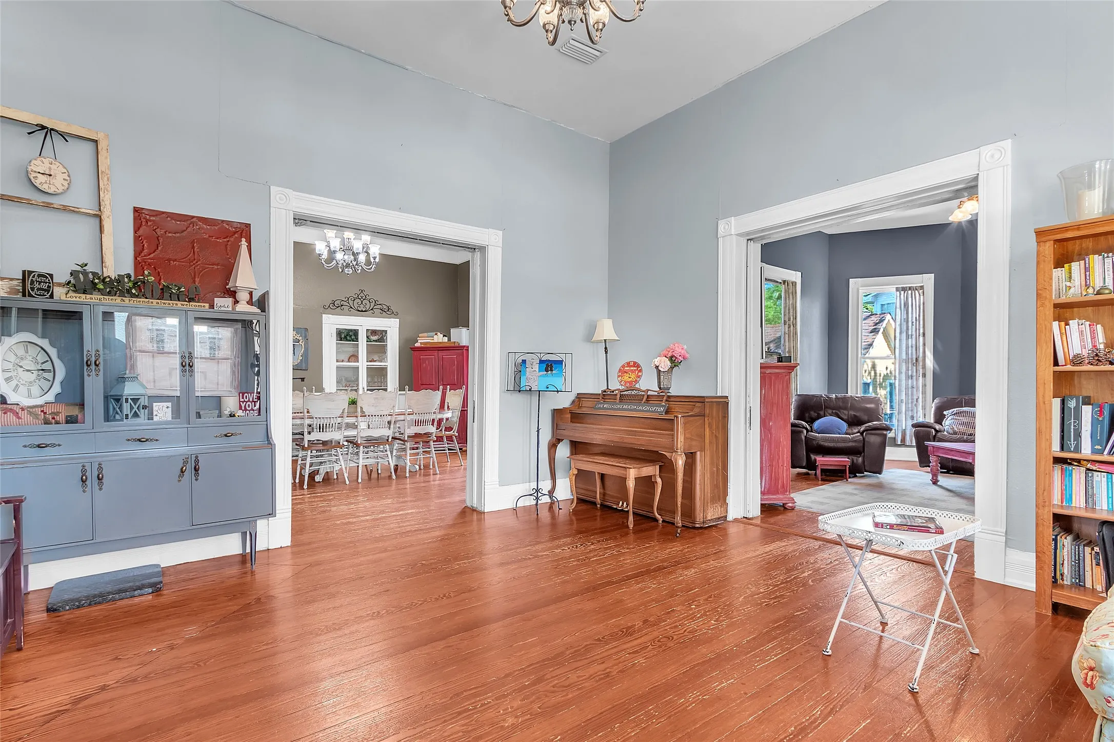 Living room with hardwood flooring, large windows allowing natural light, and an open layout leading to the dining area and piano ??.