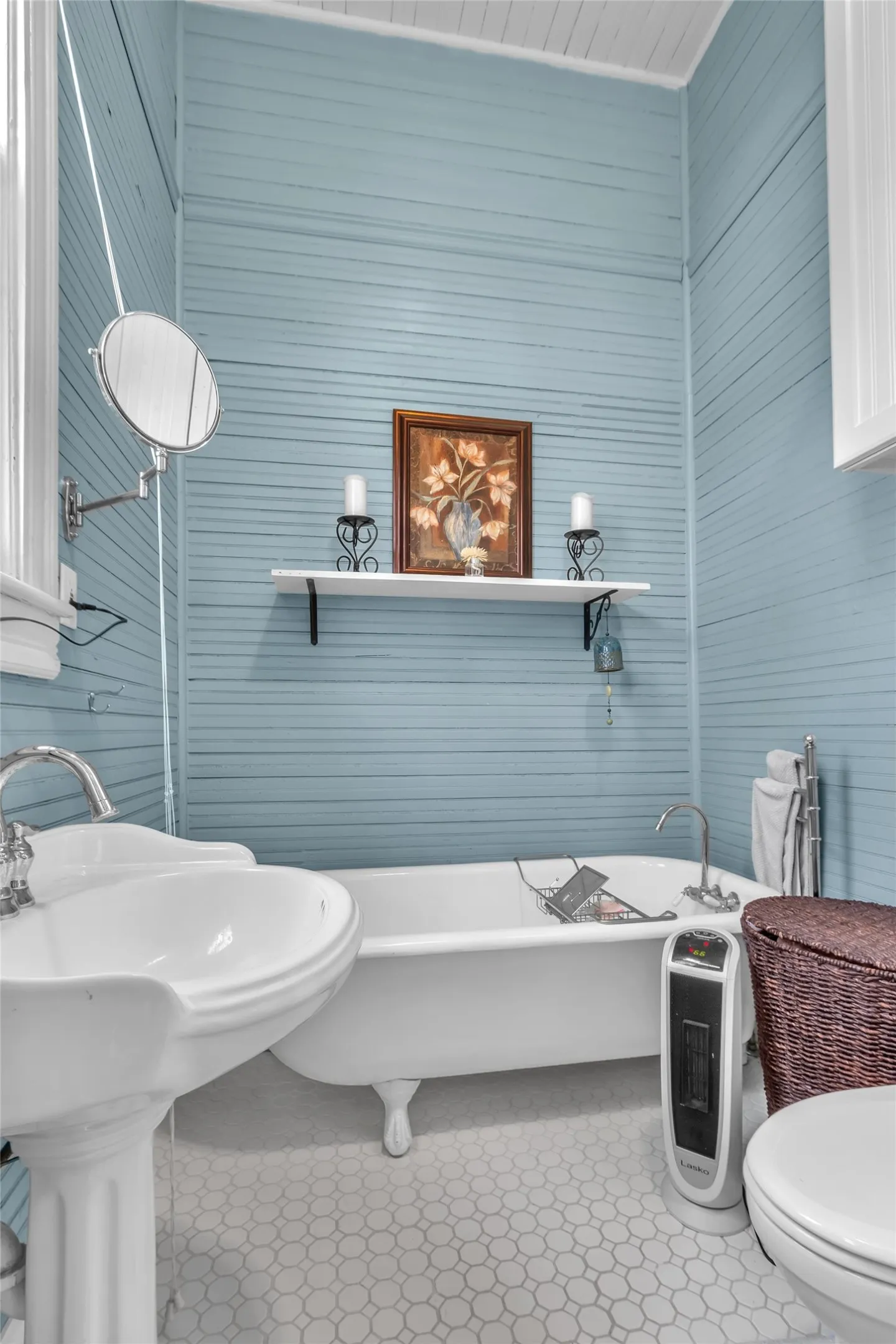 Bathroom with clawfoot tub, pedestal sink, white hexagonal tiles, shiplap walls in light blue, and a decorative wall-mounted shelf