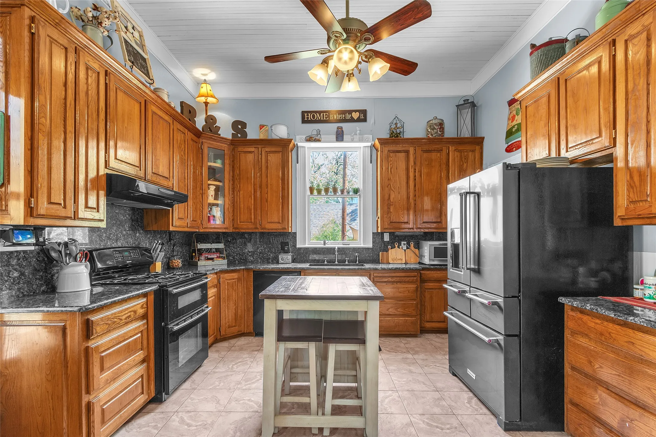 Open-plan kitchen with oak cabinetry, black granite countertops, stainless steel appliances, and central island illuminated by natural light from a window