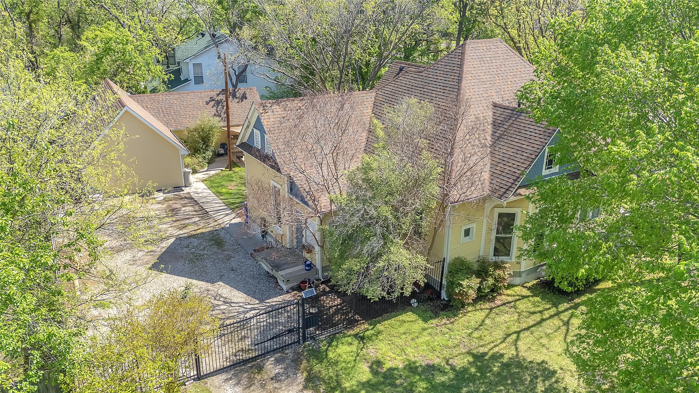 Two-story residence with a mix of siding and shingles, surrounded by mature trees, featuring a gravel driveway and gated entry.