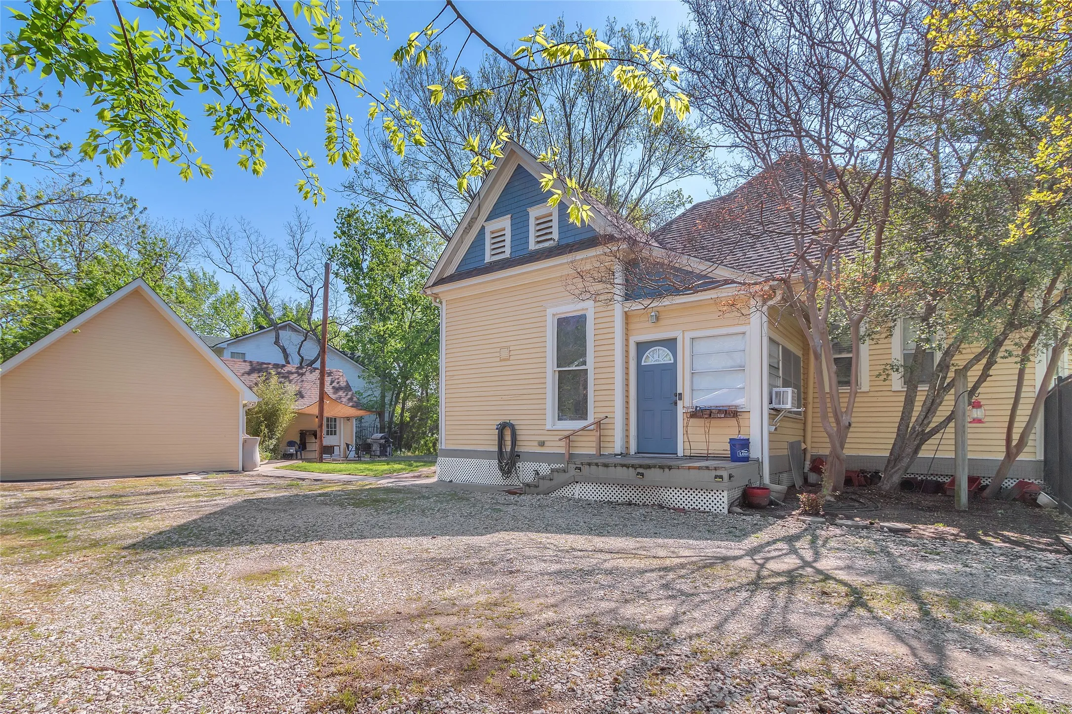 Front exterior of a two-story historic home with yellow siding, blue door, decorative trim, and a gravel driveway under clear blue skies