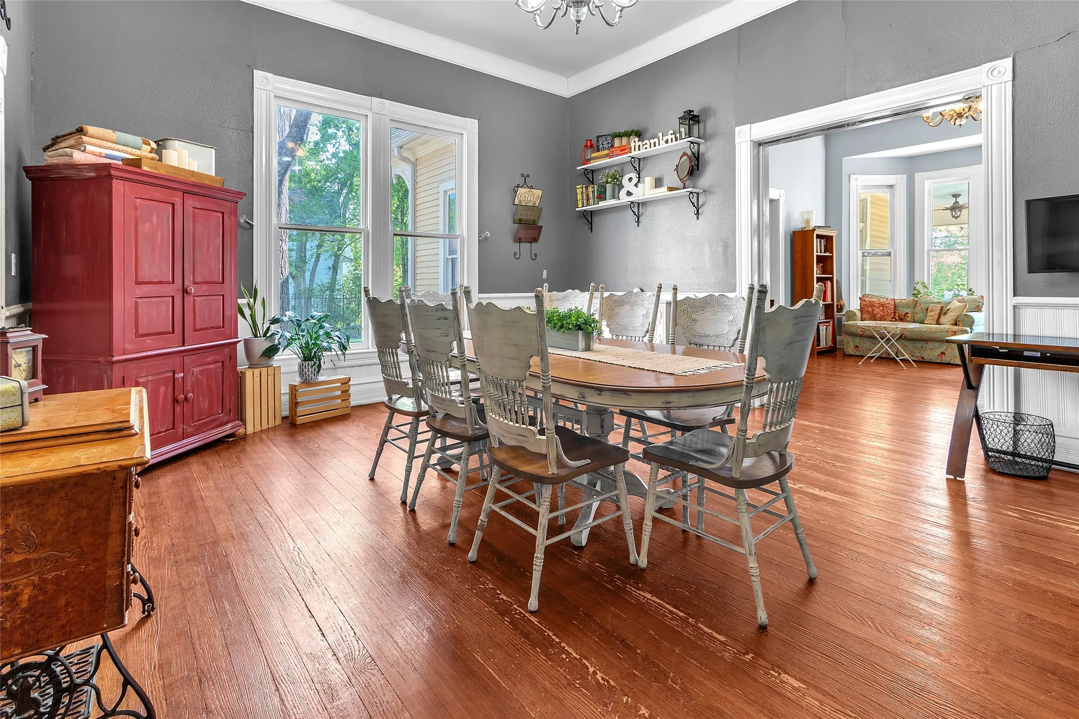 Dining room with a large wooden table surrounded by wooden chairs, hardwood flooring, and windows providing natural light, open to adjacent living space.