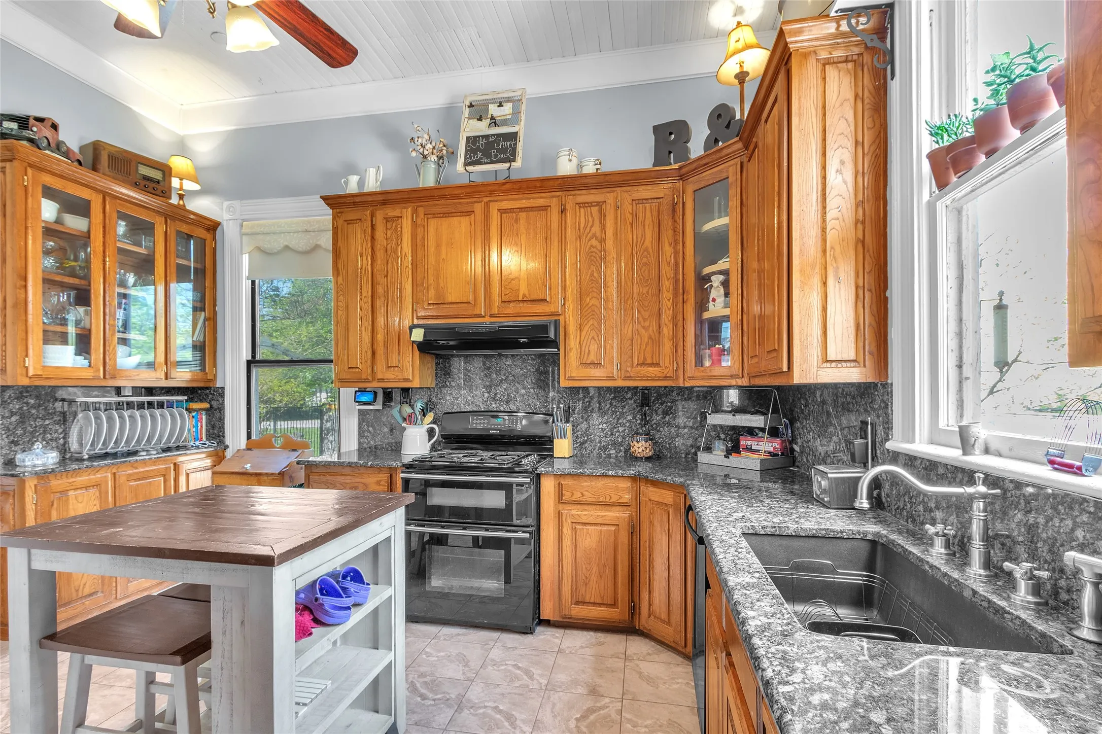 Open-plan kitchen with oak cabinetry, granite countertops, stainless steel appliances, large window for natural light, and tiled flooring.