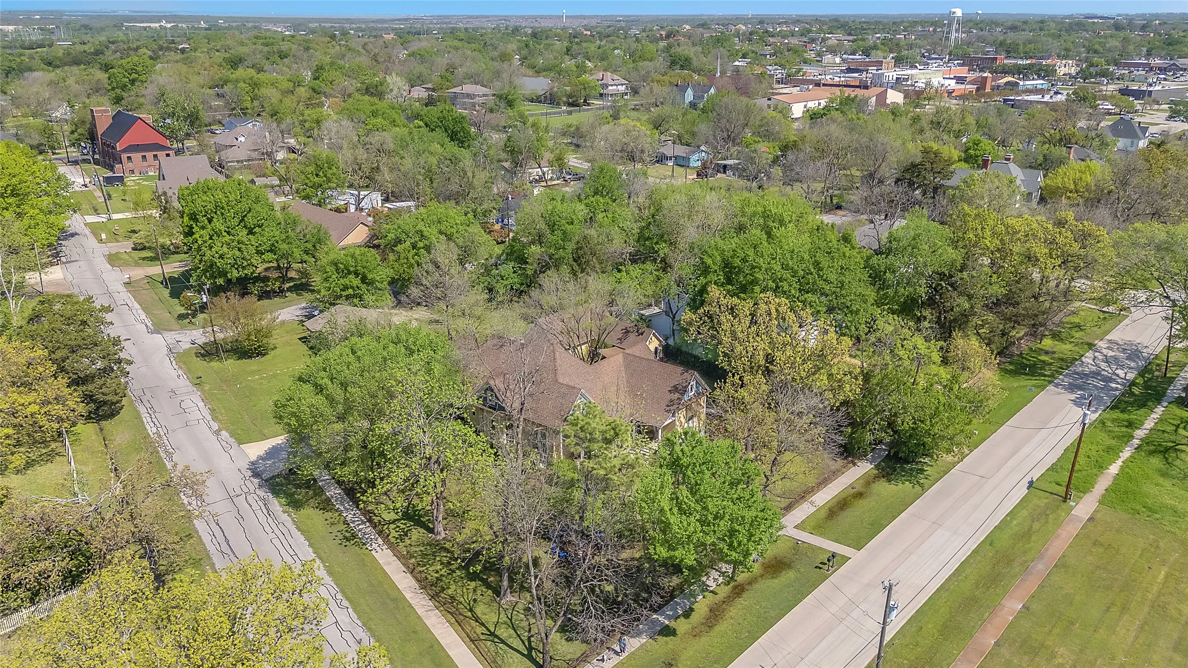 Aerial view of landscaped lot with mature trees, paved streets, and residential homes in a suburban neighborhood, showcasing green space and proximity to amenities