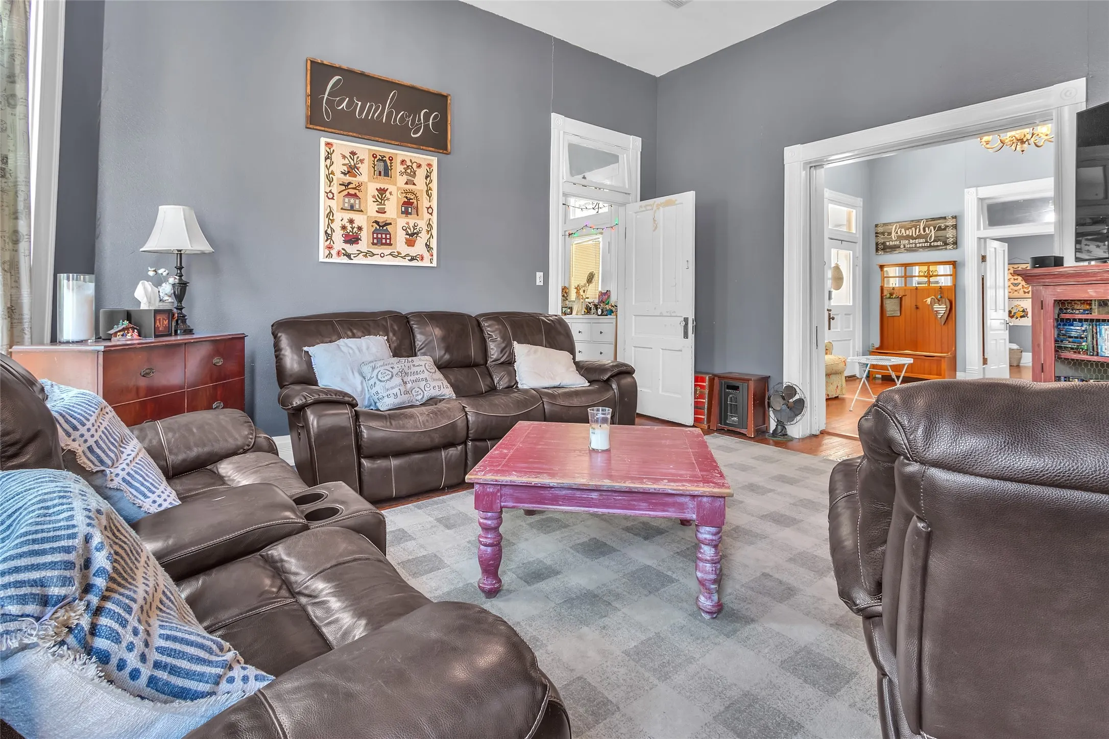 Living room with leather seating, a purple wooden coffee table, textured gray carpet, and light from adjacent rooms illuminating the open layout