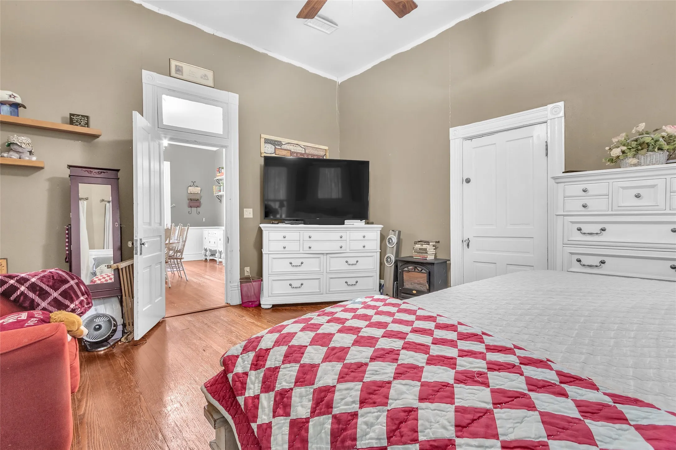 Primary bedroom with hardwood flooring, white cabinetry, and exposed wood beam ceiling, illuminated by natural light from adjacent room doorway.