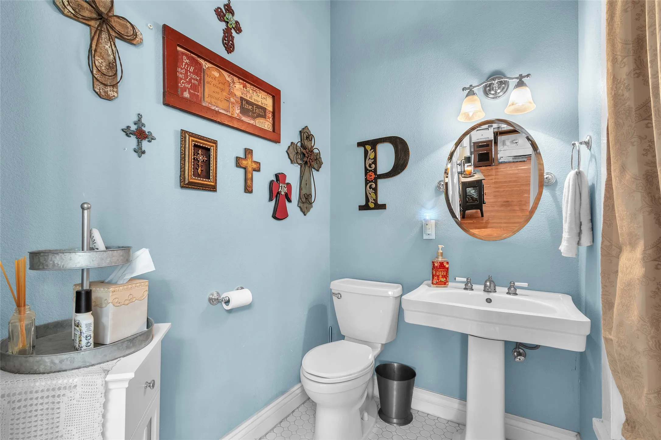 Half bathroom with ceramic tile flooring, light blue walls, chrome fixtures, and decorative wall art including crosses and letters.