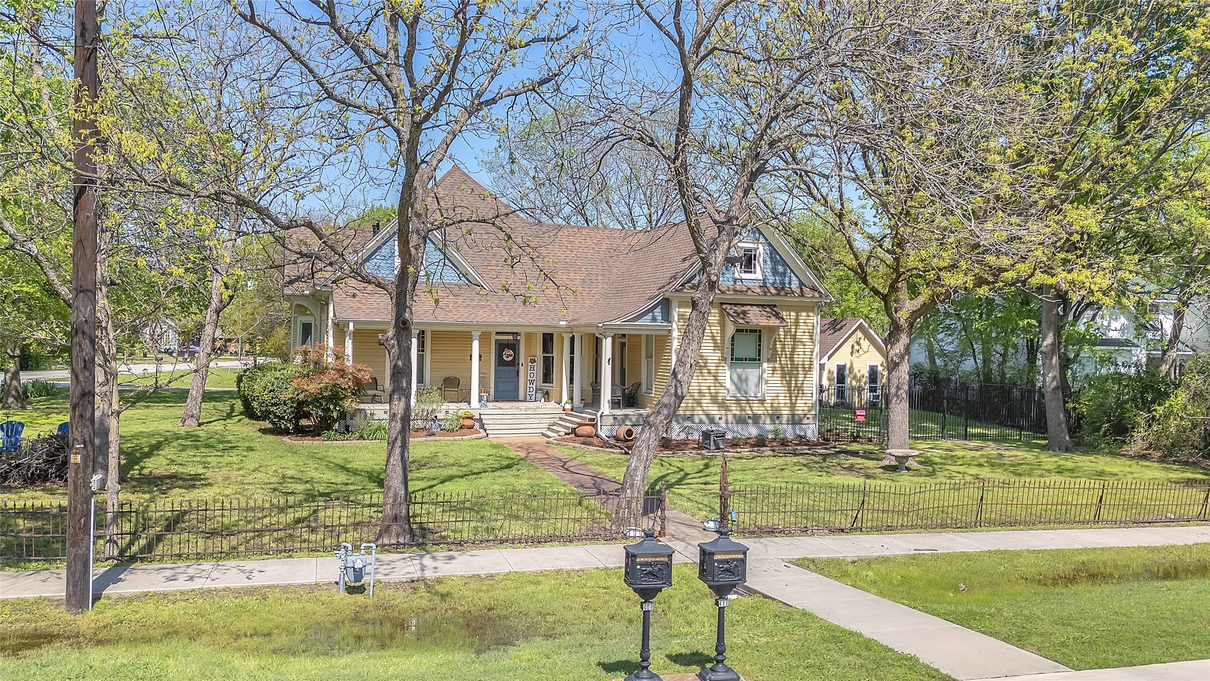 Victorian-style home with a wraparound porch, a gabled roof, and a fenced yard, surrounded by mature trees and landscaped grounds.
