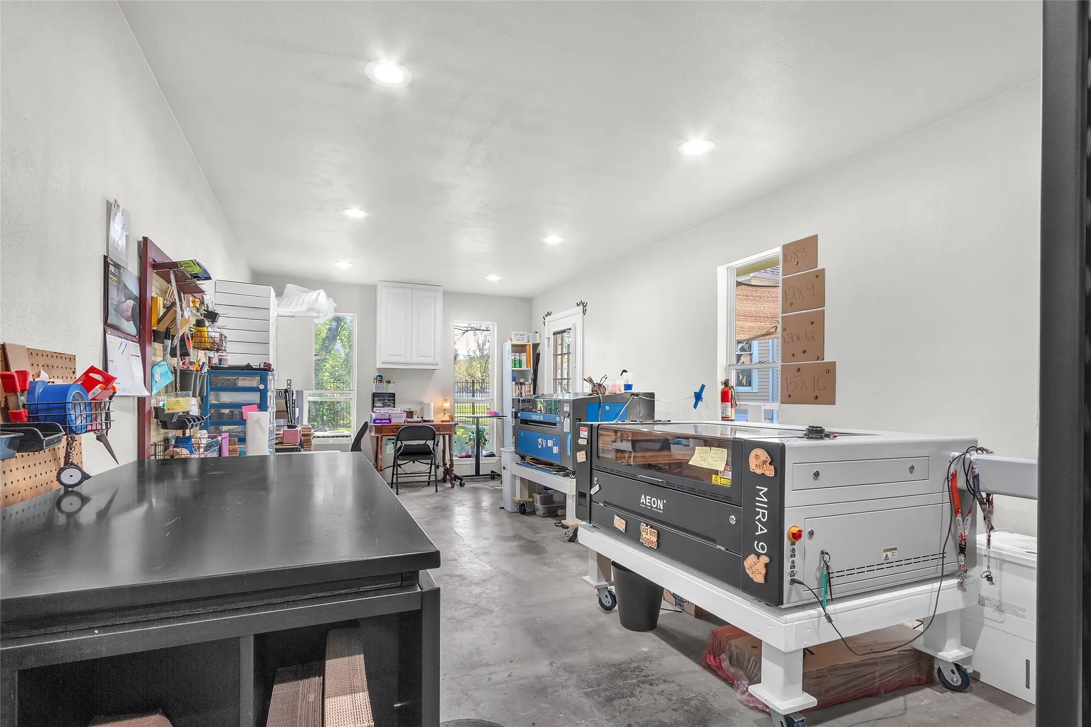 Bright workshop with concrete flooring, organized shelving, multiple workstations, and recessed lighting, providing ample space for projects and activities