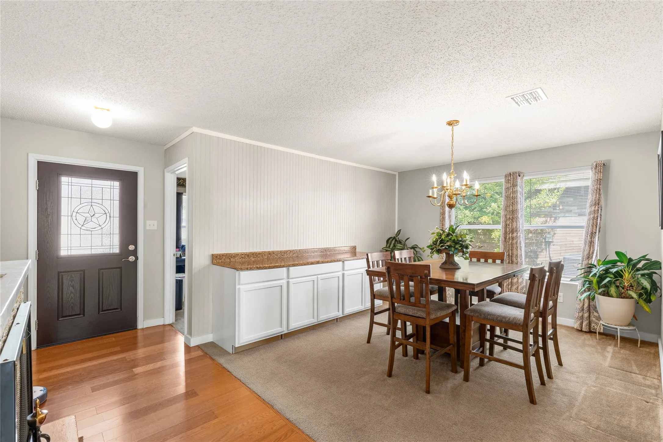 Wood-finish flooring, dark-stained entry door with leaded glass insert, built-in lower cabinetry with stone-finish countertop, and double windows