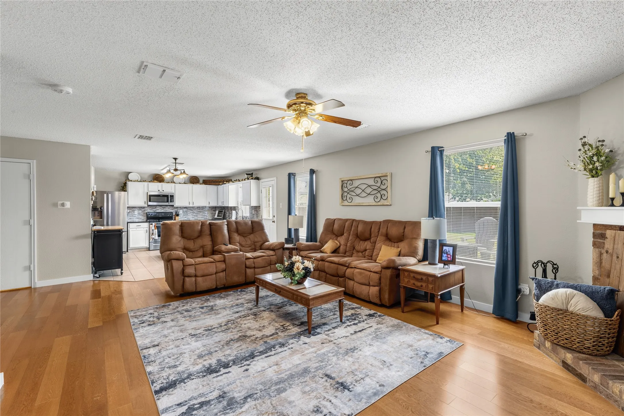 Open-concept living area with wood-finish flooring, a ceiling fan, and a brick-finish fireplace