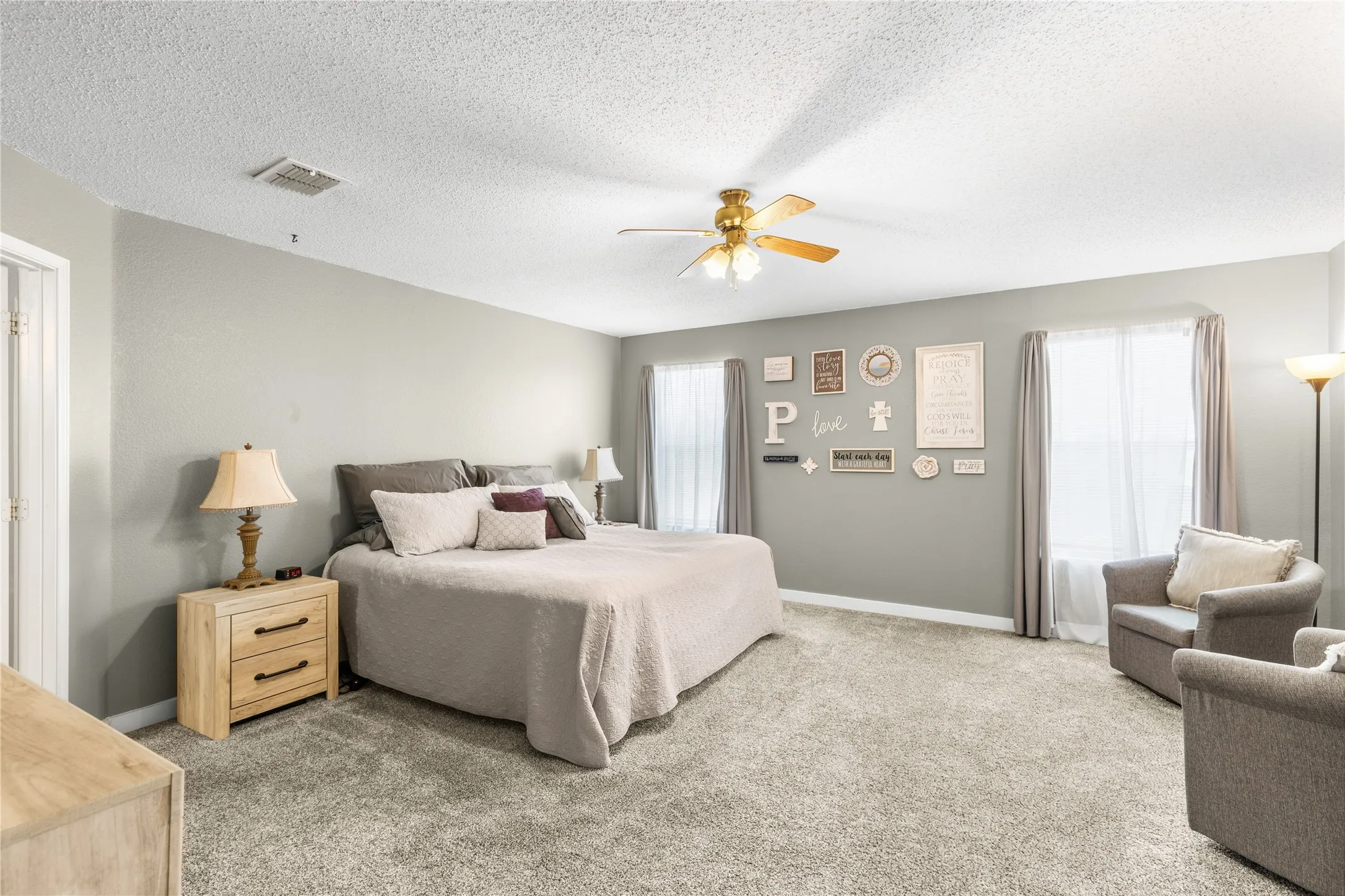 Spacious room featuring neutral carpeting, a ceiling fan, and multiple windows with curtain rods