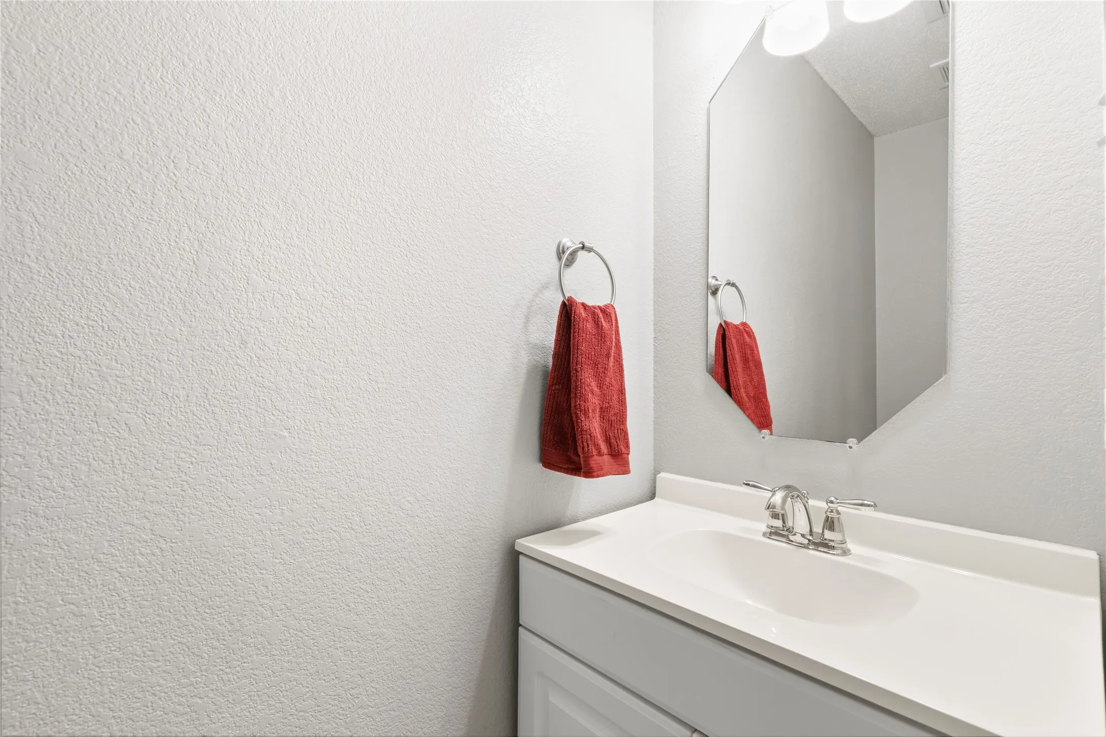 Vanity with integrated sink, brushed nickel faucet, and an octagonal frameless mirror