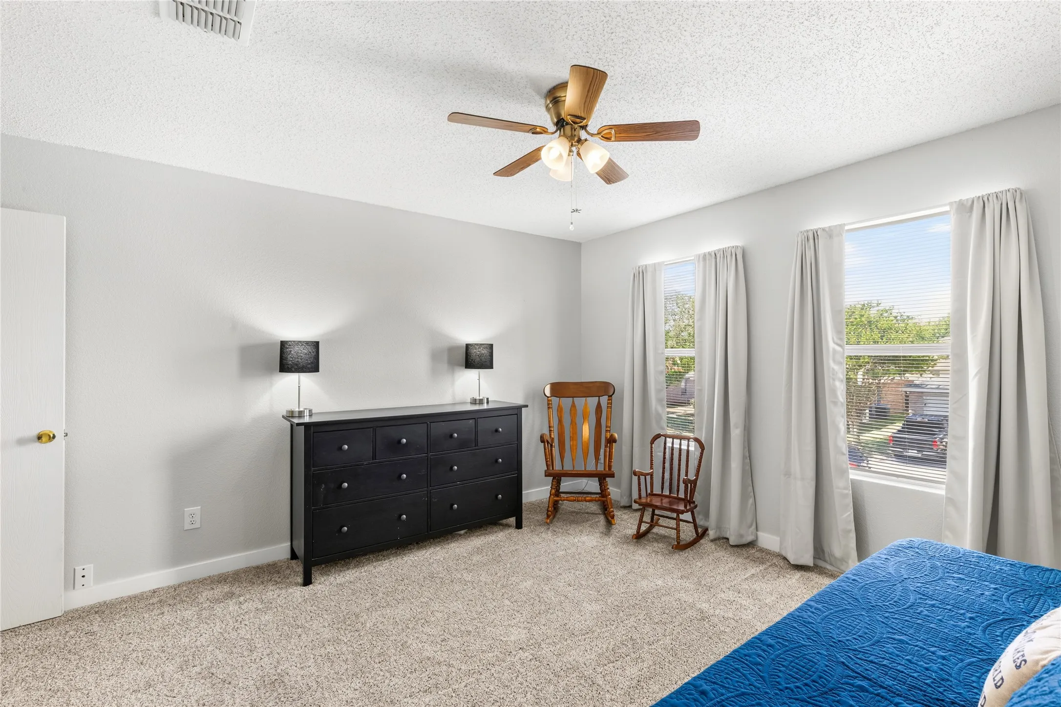 Light-colored wall paint, textured ceiling, two windows, ceiling fan with light fixture, and carpet flooring