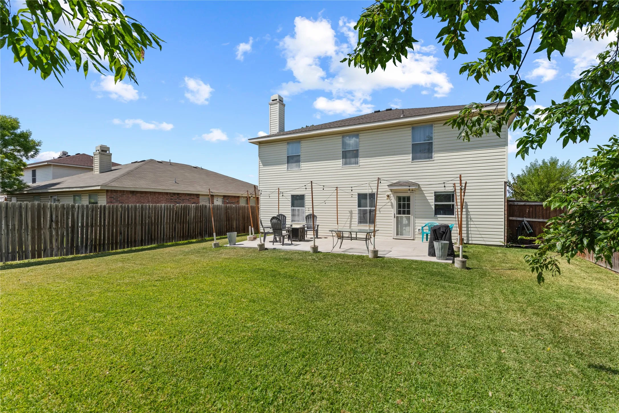 Expansive lawn with a concrete patio, privacy fencing, and two-story exterior