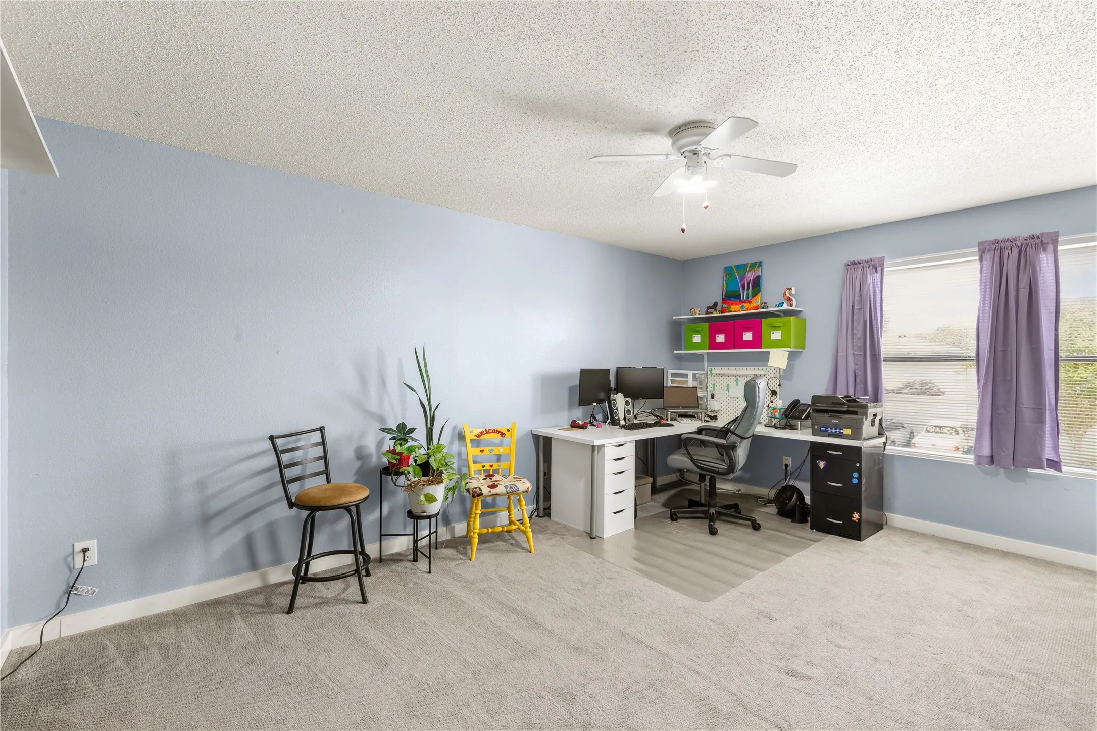 Spacious room featuring light blue walls, gray carpeting, a large window, and a ceiling fan