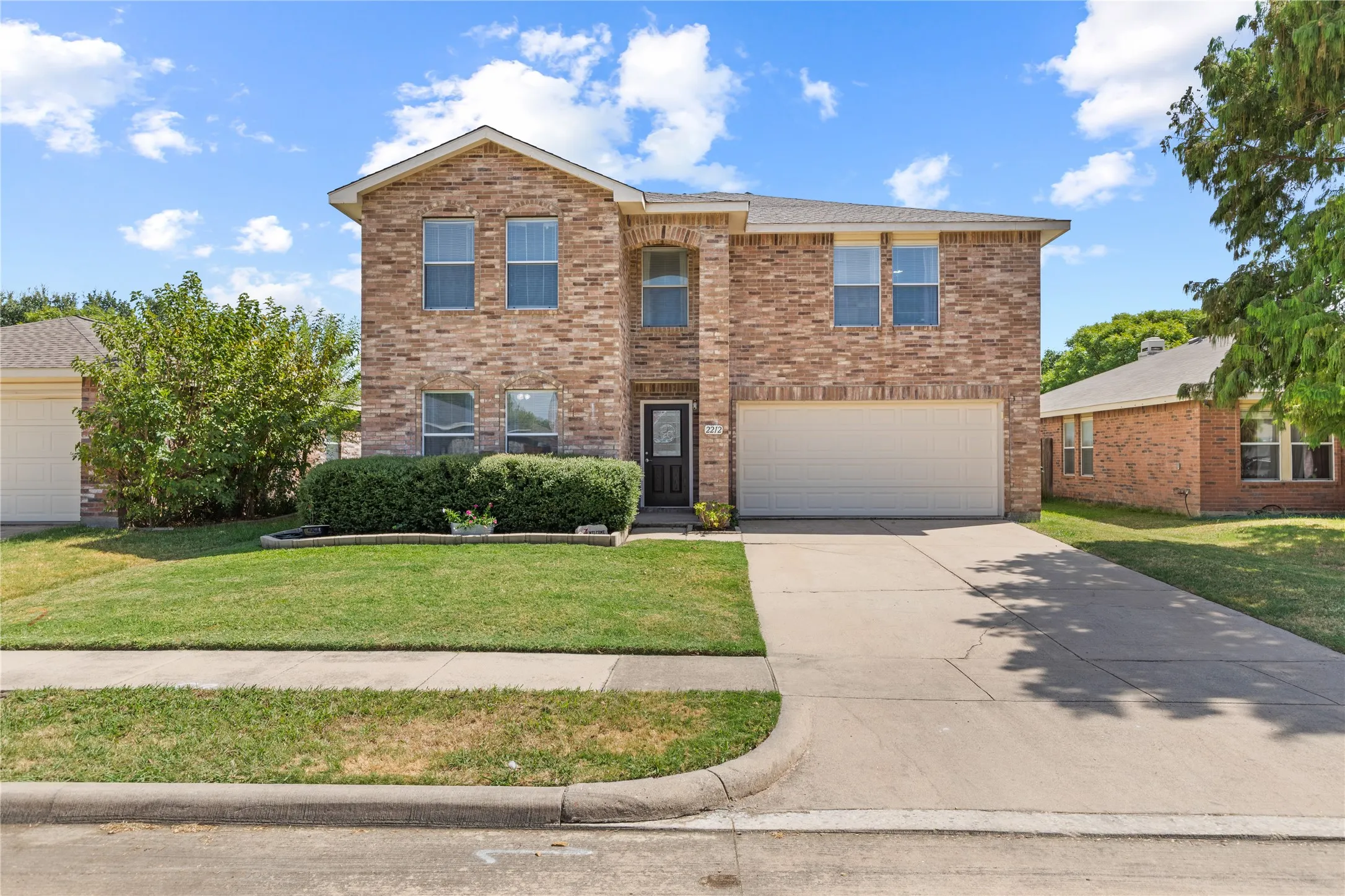 Two-story brick exterior with an attached garage, concrete driveway, and front lawn