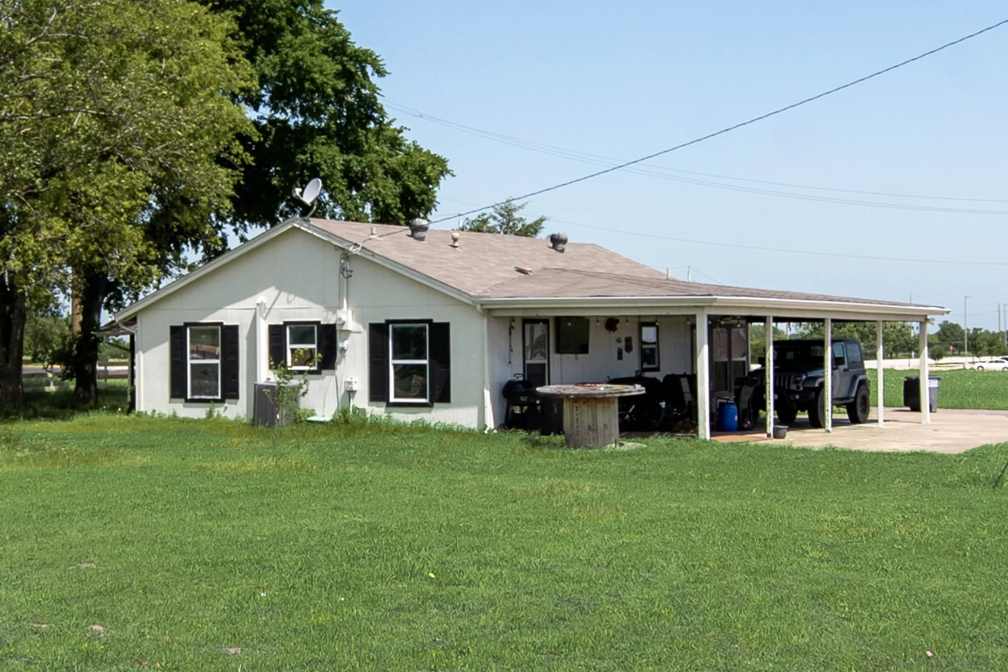 White exterior with black shutters, covered carport, and a brown shingle roof