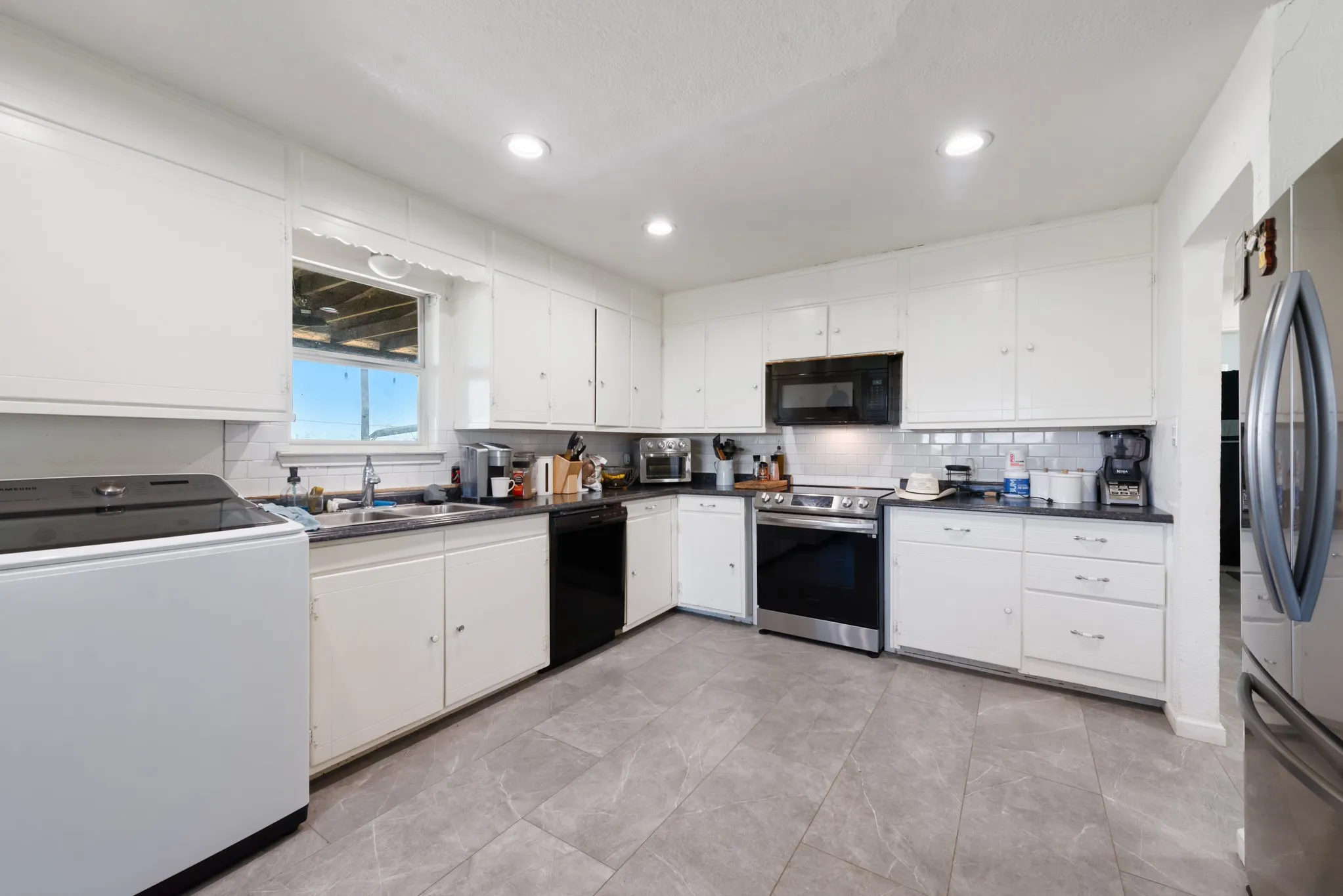 White cabinetry with black countertops, stainless steel appliances, tile flooring, and recessed lighting