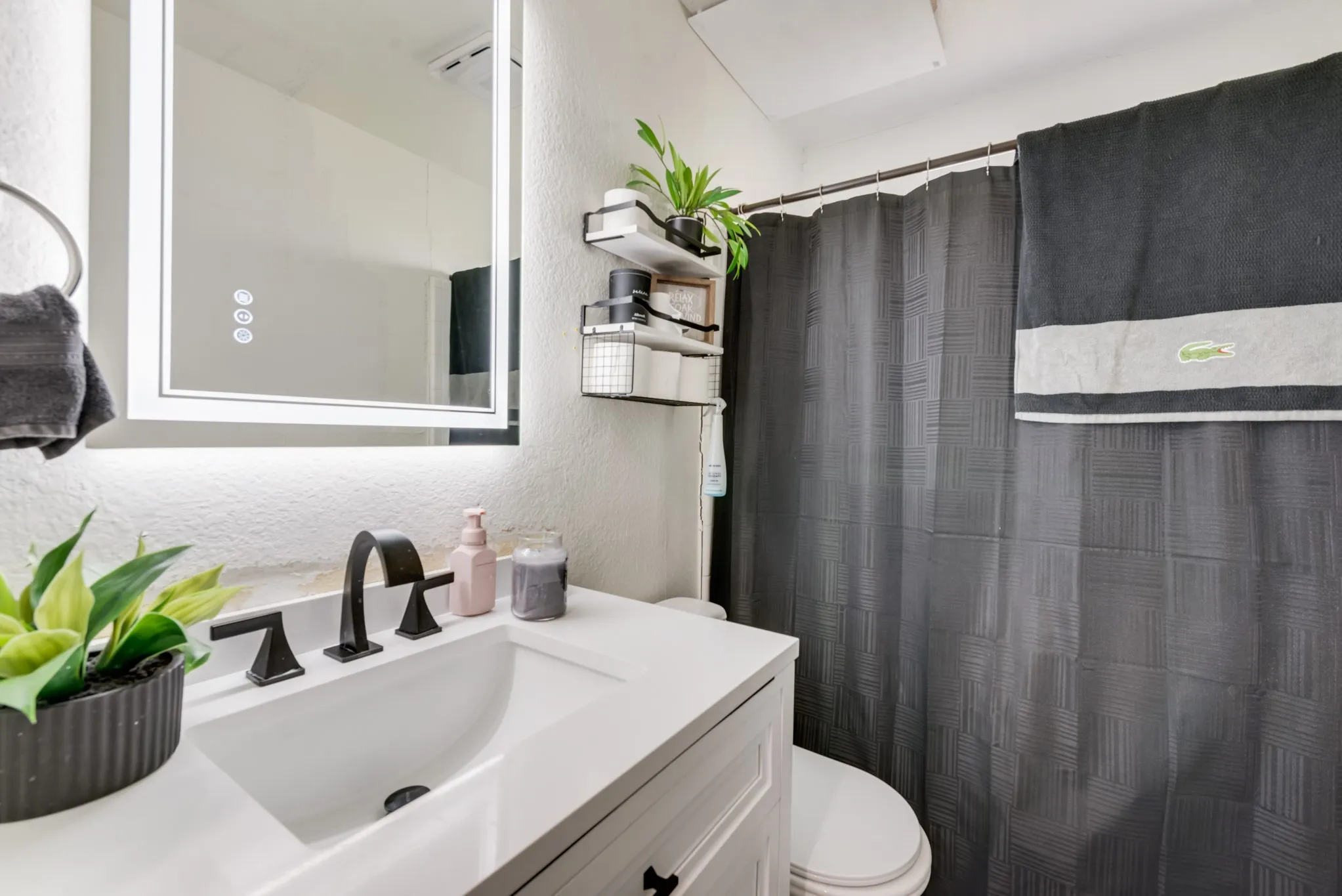 Modern vanity with integrated sink, black widespread faucet, backlit mirror, and built-in shelving