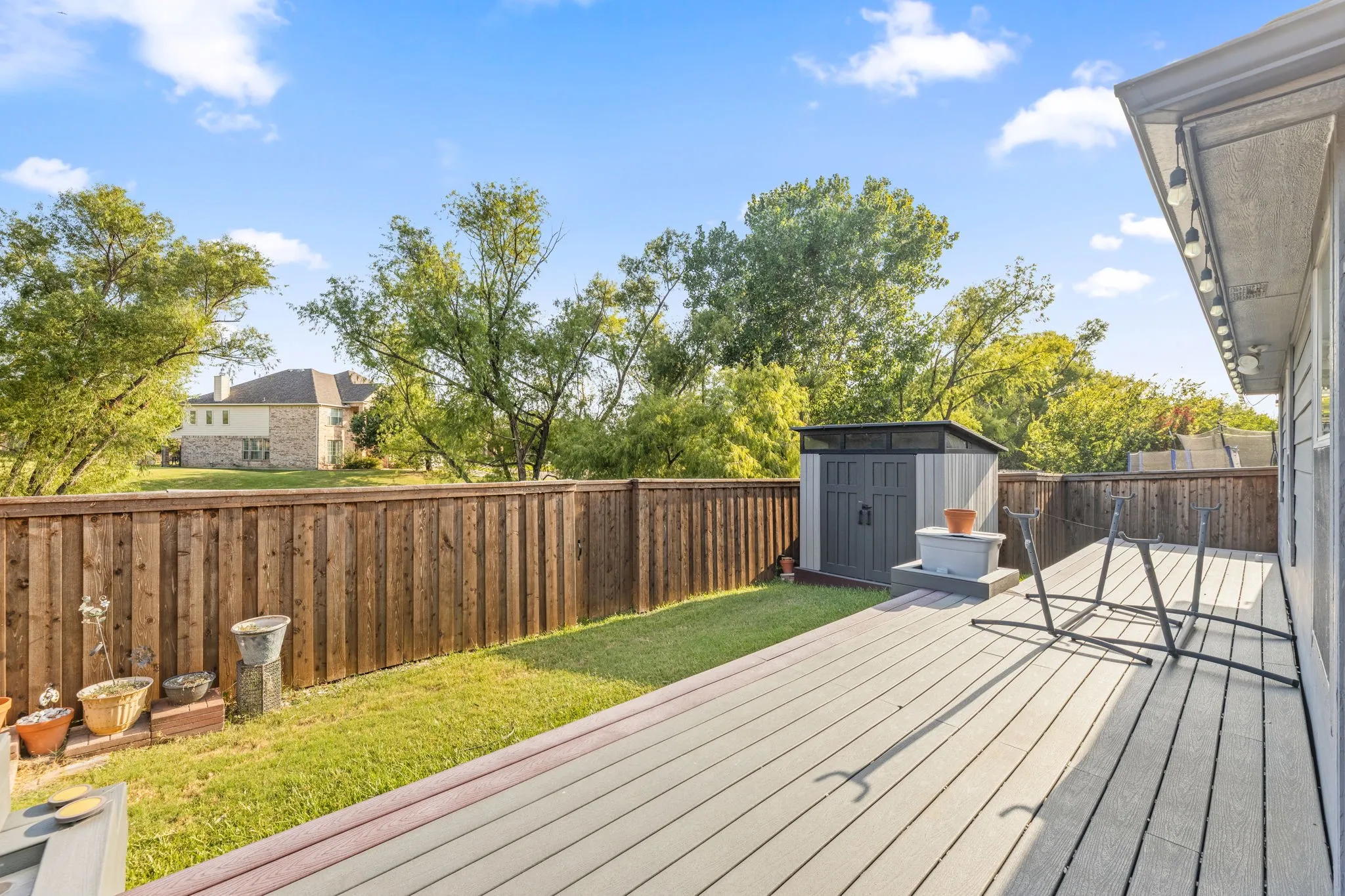 Spacious composite deck with wood-finish decking and metal railings overlooking a manicured lawn bordered by wooden privacy fencing