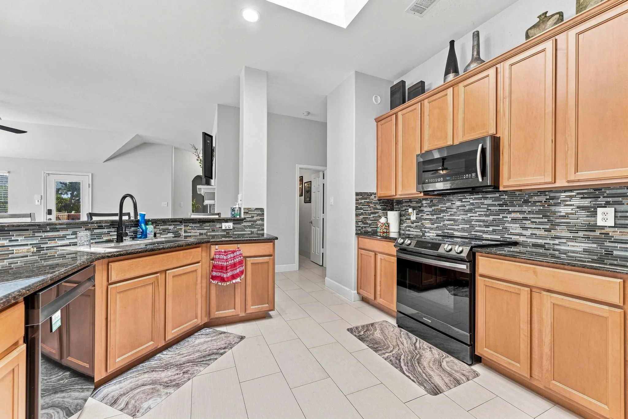 Spacious kitchen featuring warm wood-finish cabinetry, stainless steel appliances including a gas range and microwave, dual-basin sink with blue accent faucet, and a large island with seating