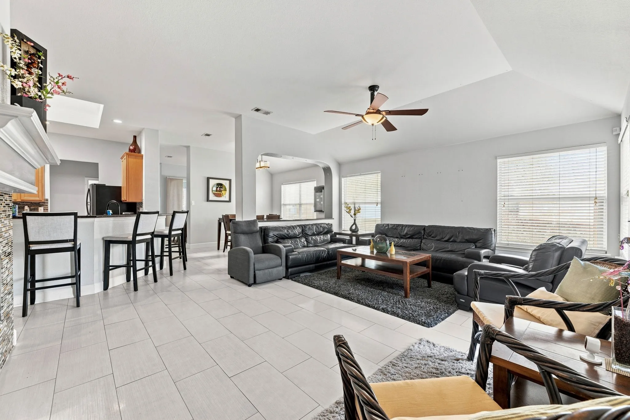 Spacious living area featuring light-toned tile flooring, tray ceiling, and a ceiling fan