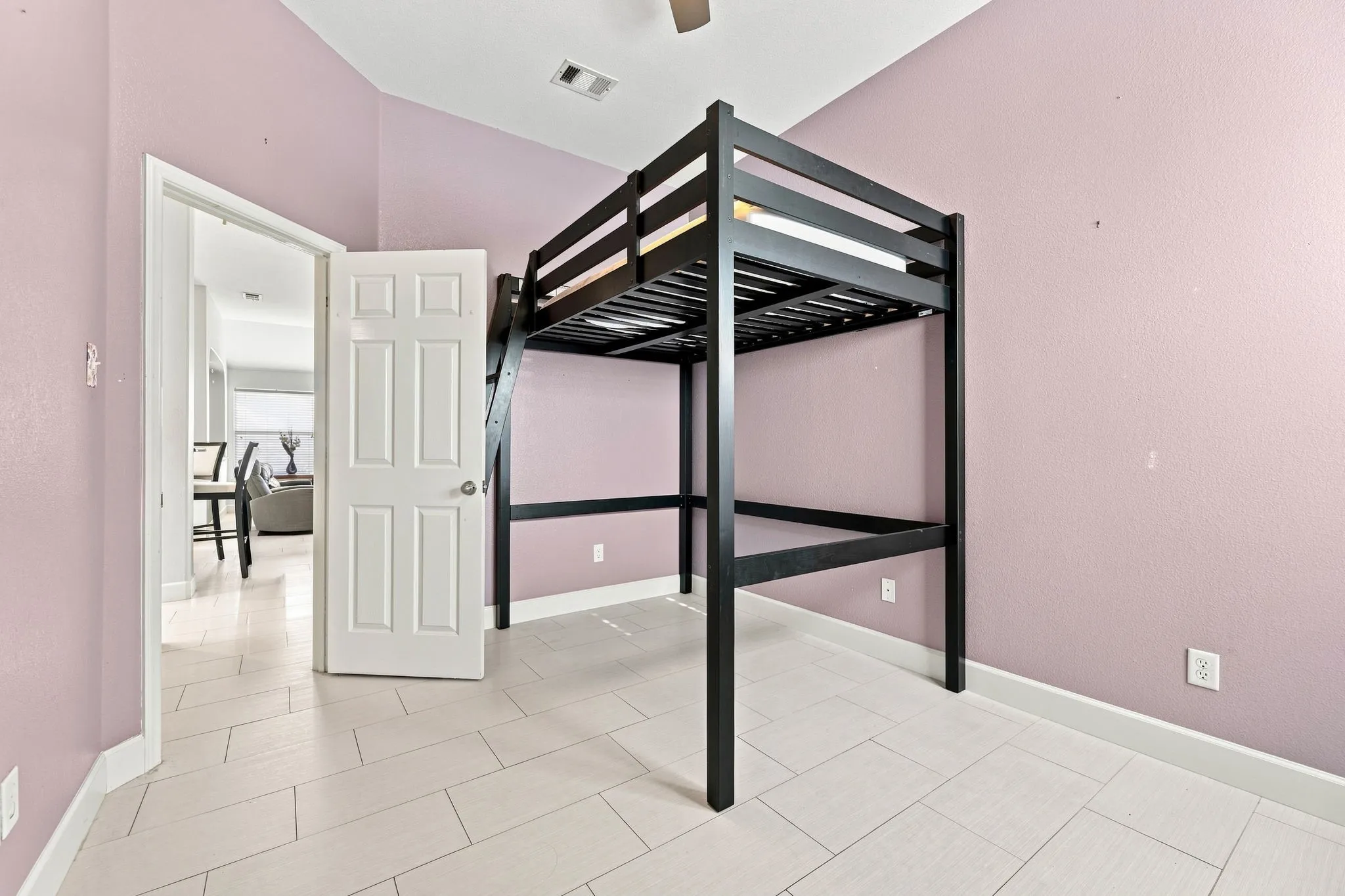 Spacious bedroom showcasing a black metal loft bed frame with slatted support, neutral tile flooring, and soft mauve walls