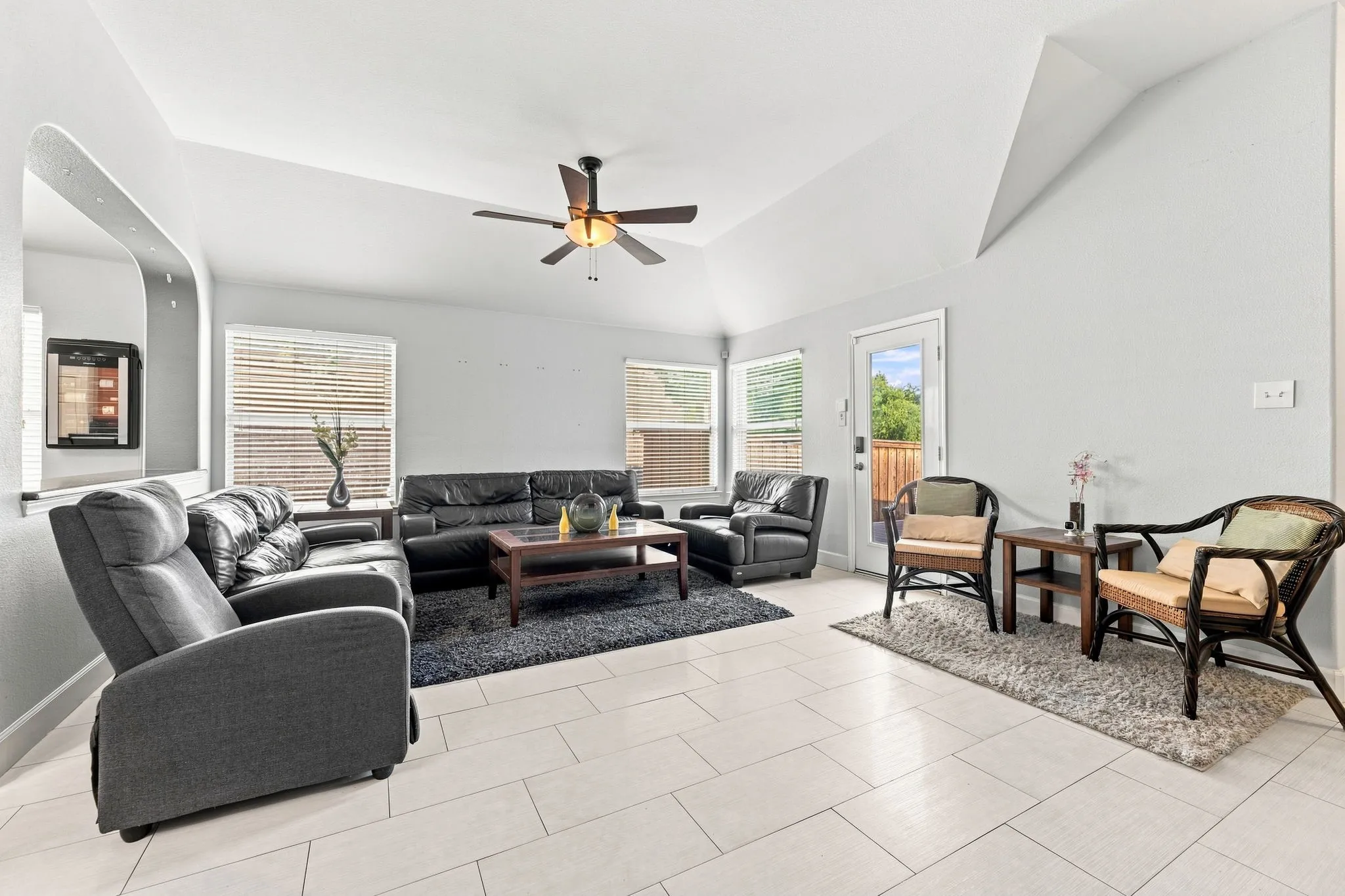 Spacious living area showcasing vaulted ceilings, neutral tile flooring throughout, and abundant natural light from multiple windows and glass doors