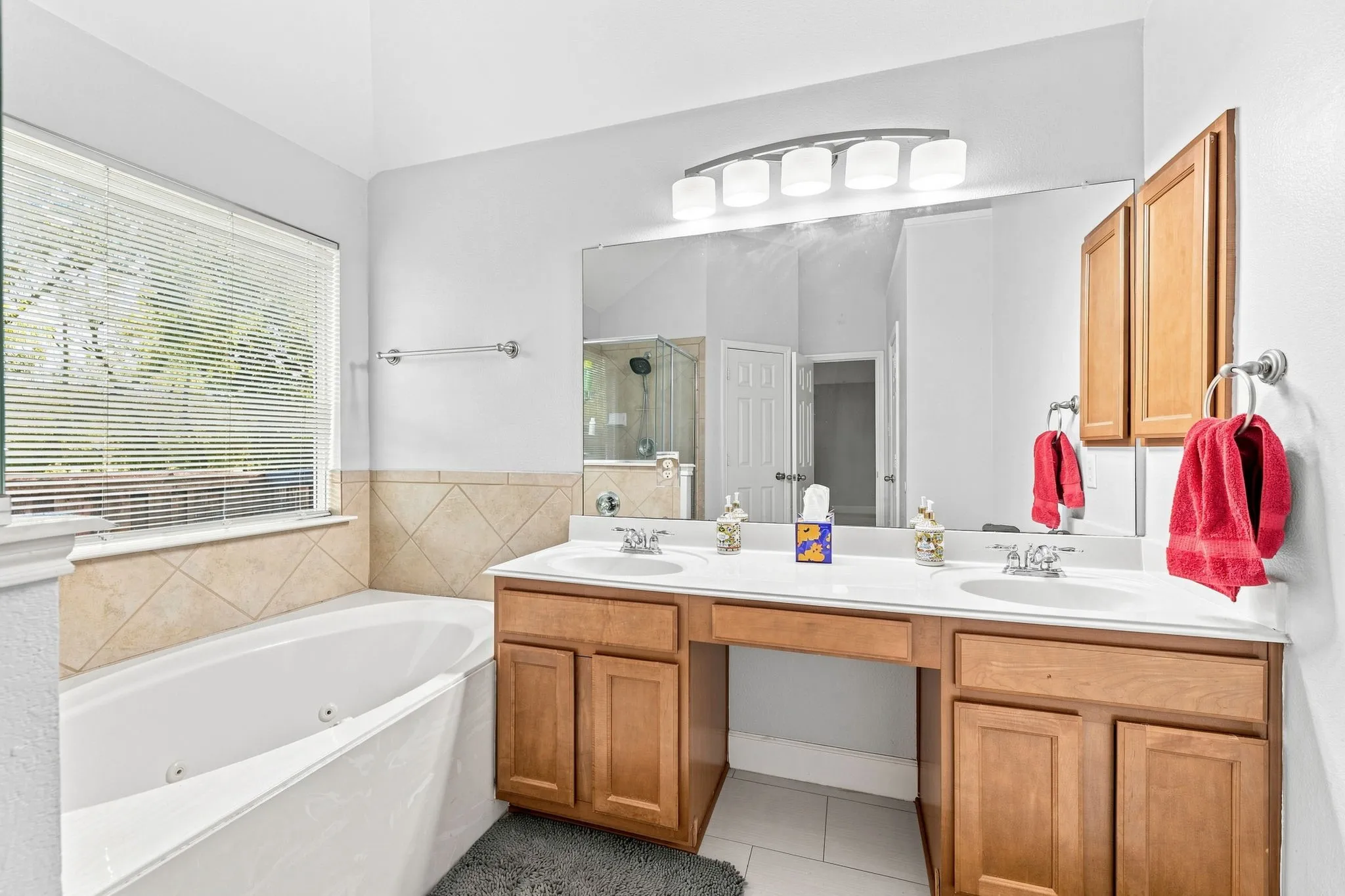 Spa-inspired primary bathroom featuring dual vanities with wood cabinetry, white quartz countertops, and polished chrome fixtures