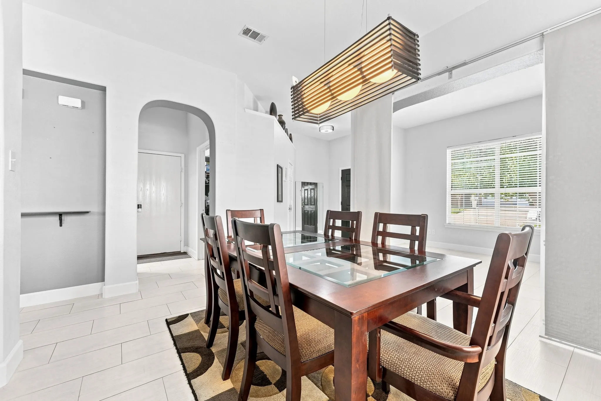 Bright dining area featuring a wood-finish table with seating for six, white subway tile flooring, recessed ceiling lighting, and a linear pendant fixture