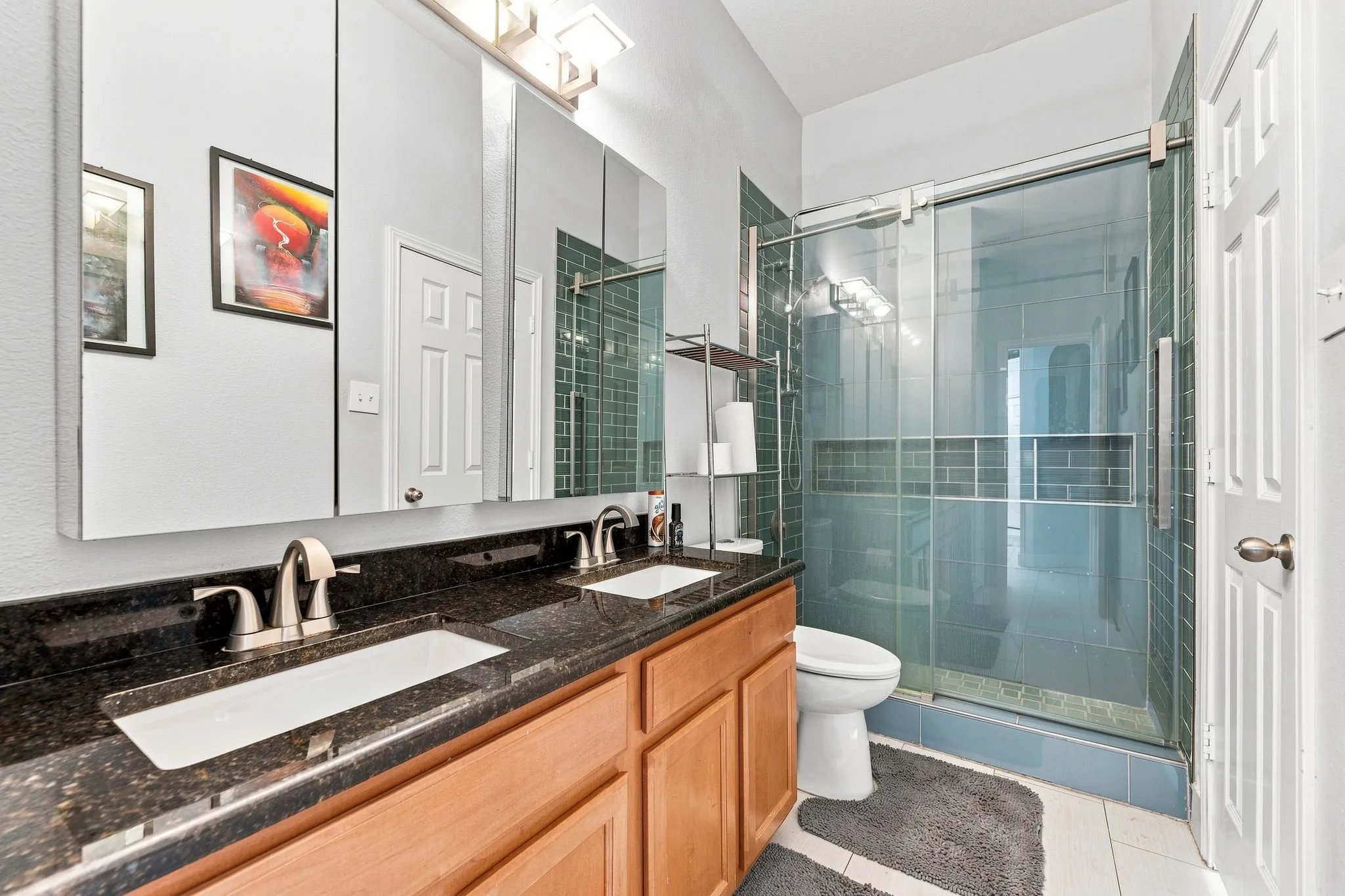 Primary bathroom featuring a wood-finish vanity with dual rectangular vessel sinks, dark stone countertop, brushed nickel faucetry, and large framed mirror