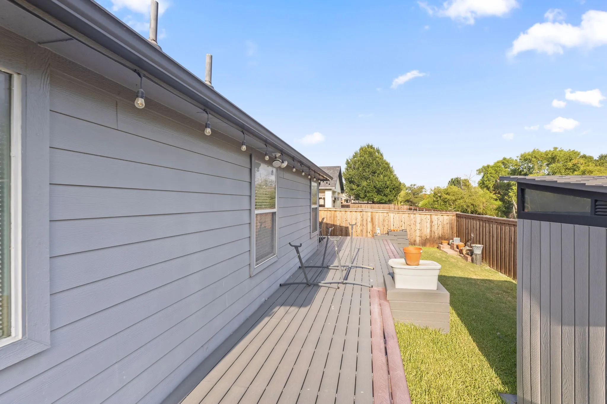 Modern composite deck with horizontal board styling spans the length of the home, featuring pendant lighting fixtures and direct access to the residence
