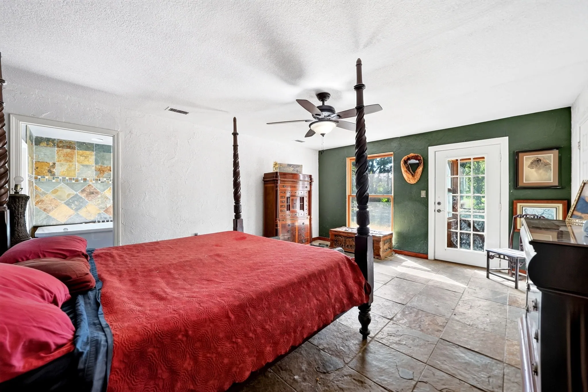Spacious primary bedroom featuring a four-poster bed frame, ceiling fan, tile flooring, and an accent wall in deep green