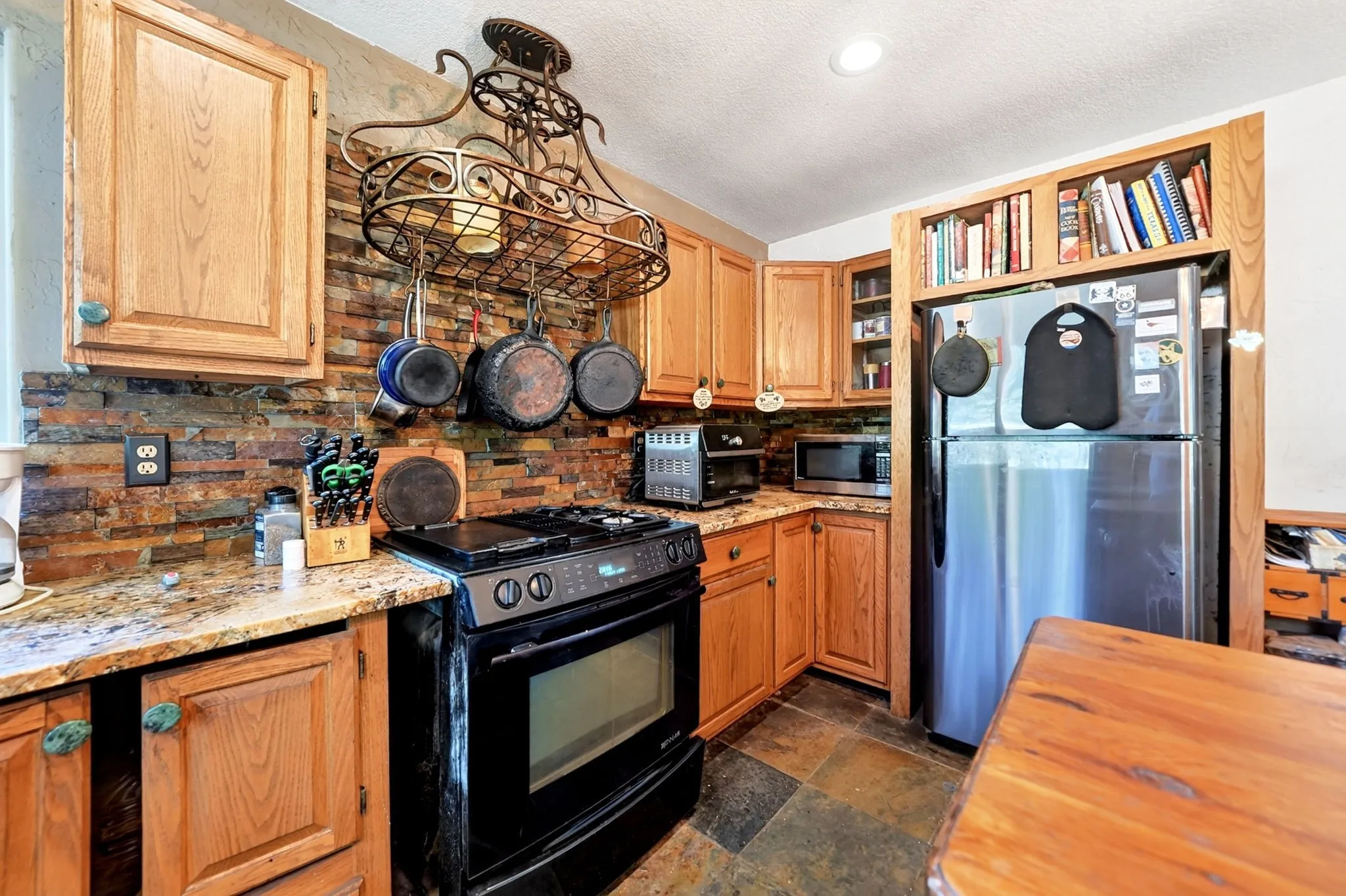 Wood cabinetry with granite-style countertops, stone tile backsplash, and slate tile flooring