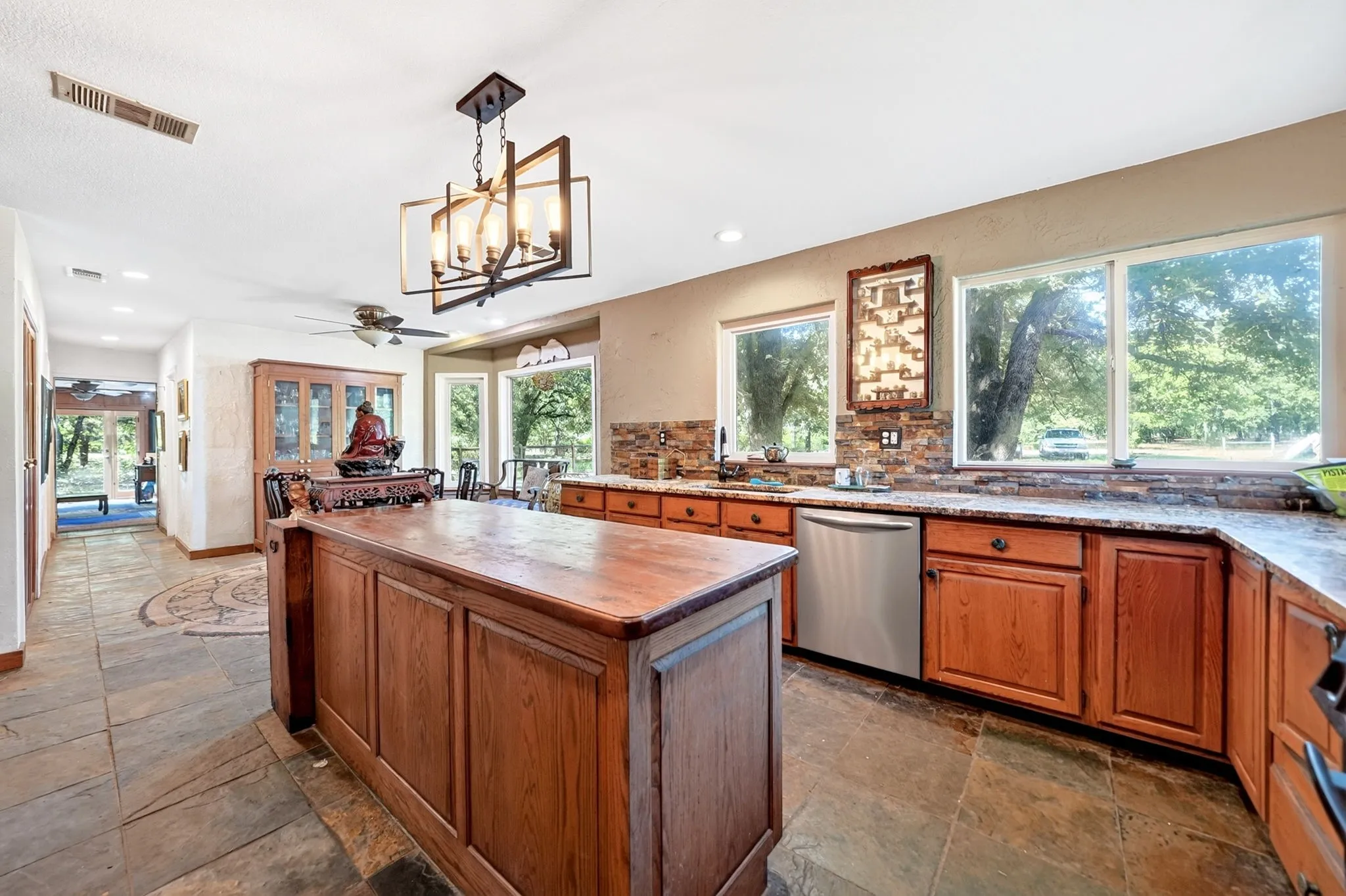 Spacious chef's kitchen featuring custom wood cabinetry, a large center island with wood-finish countertop, stainless steel appliances including a dishwasher, and abundant natural light from multiple expansive windows